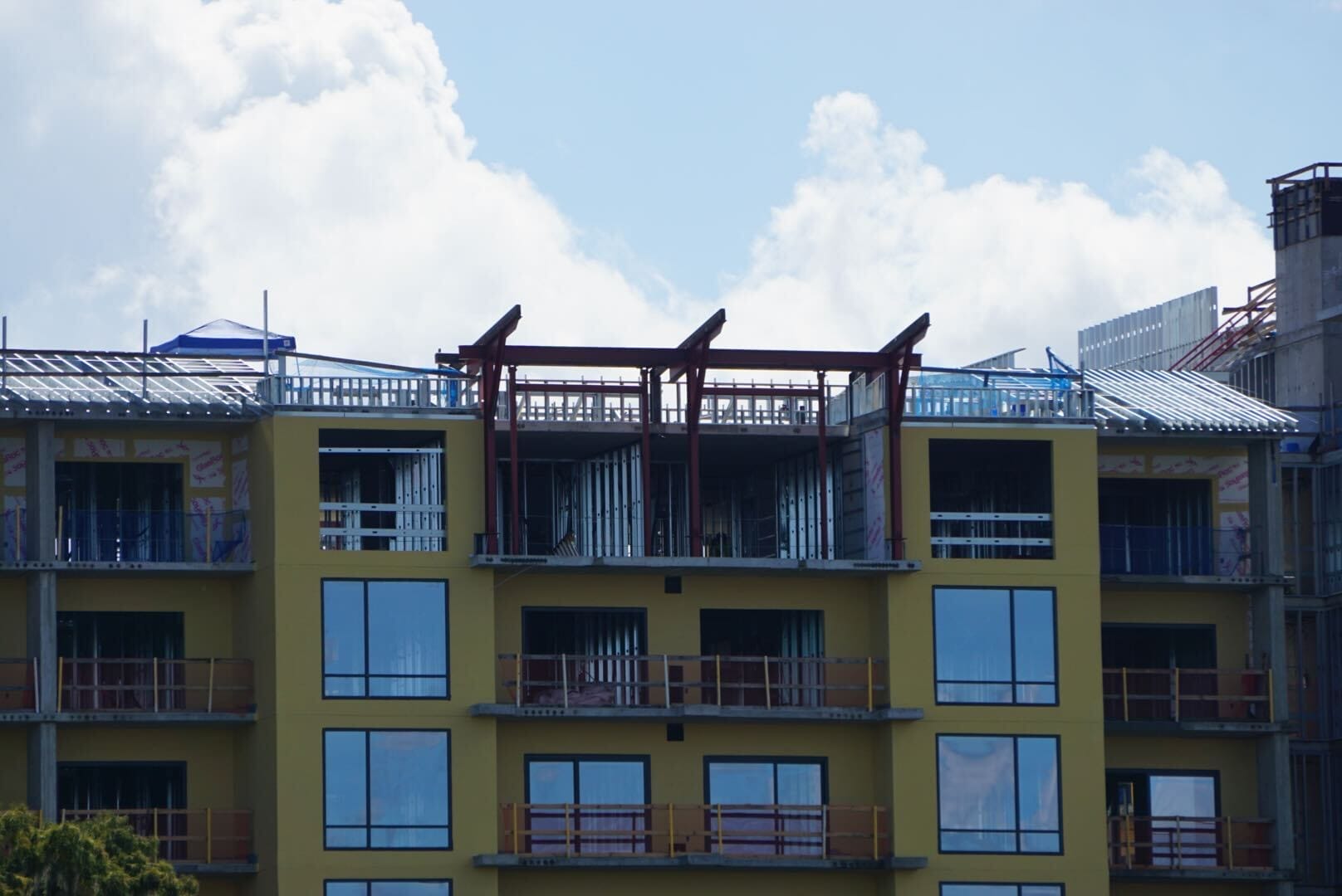 A yellow apartment building under construction near Disney Lakeshore Lodge, with scaffolding and exposed beams on top.