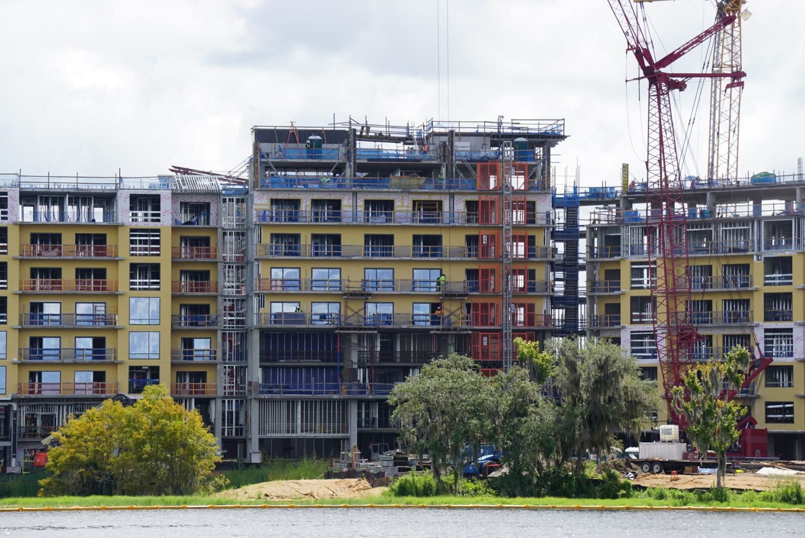 Several mid-rise apartment buildings under construction with cranes and scaffolding near a body of water.