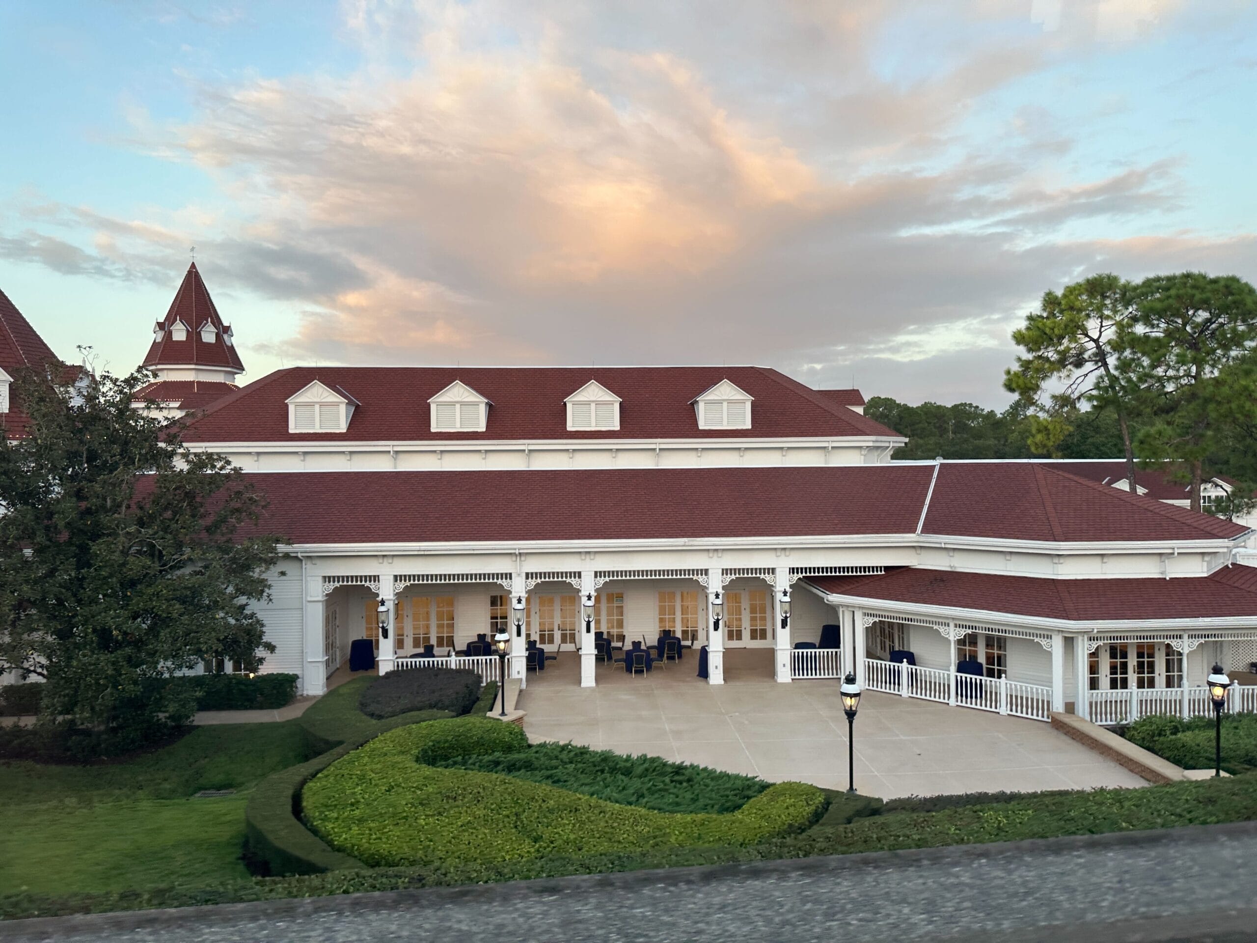 Large white building with red roof and columns, like Disney's Grand Floridian Resort, beneath a dramatic sunset sky.