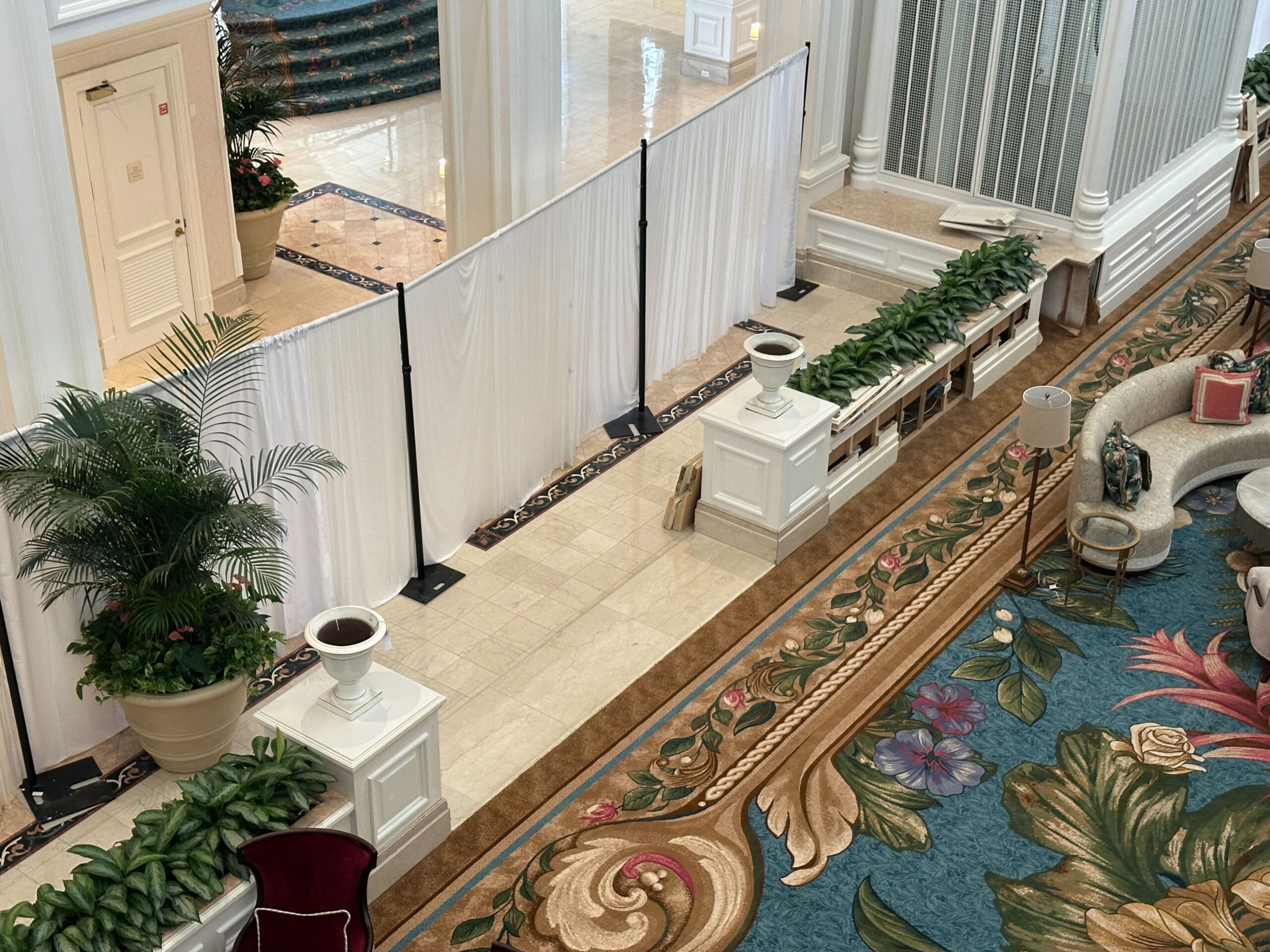 White curtains section off part of the Grand Floridian Resort lobby, featuring Disney elegance with lush plants and ornate furniture.