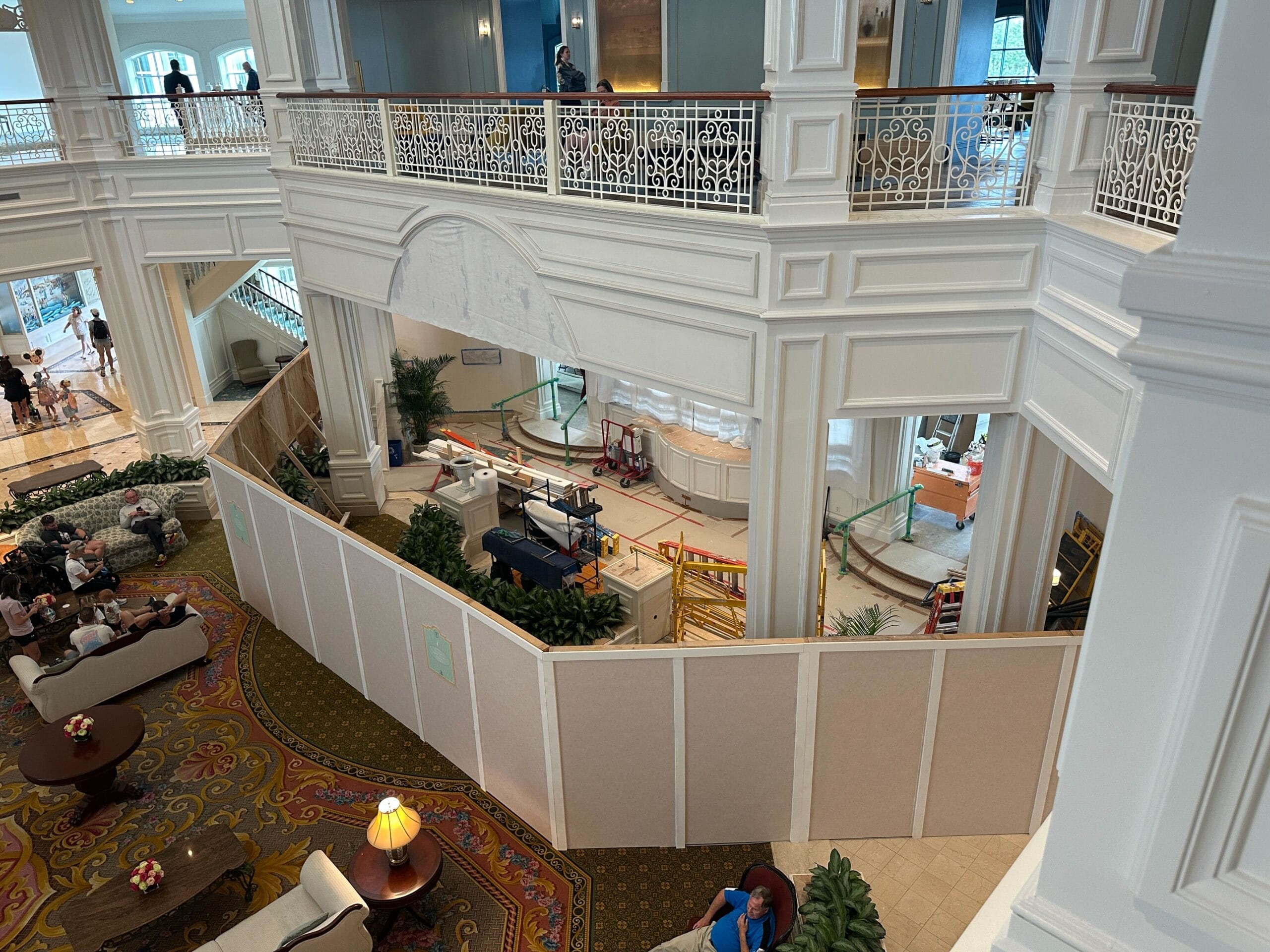 A hotel lobby at the Grand Floridian with construction barriers and decorative panels; guests are seated on couches nearby.