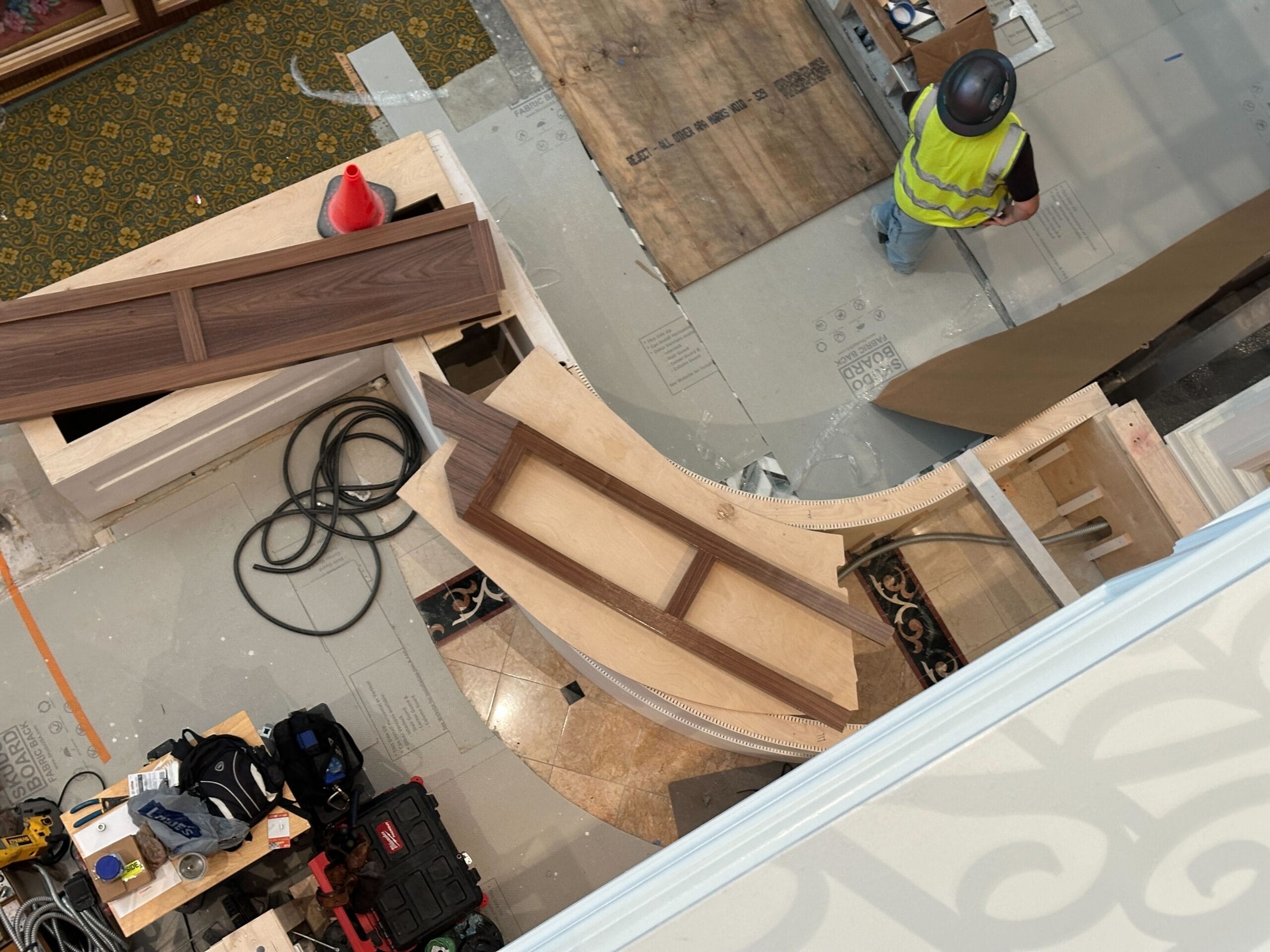A construction worker stands beside curved wood panels and tools at Disney's Grand Floridian Resort, viewed from above.