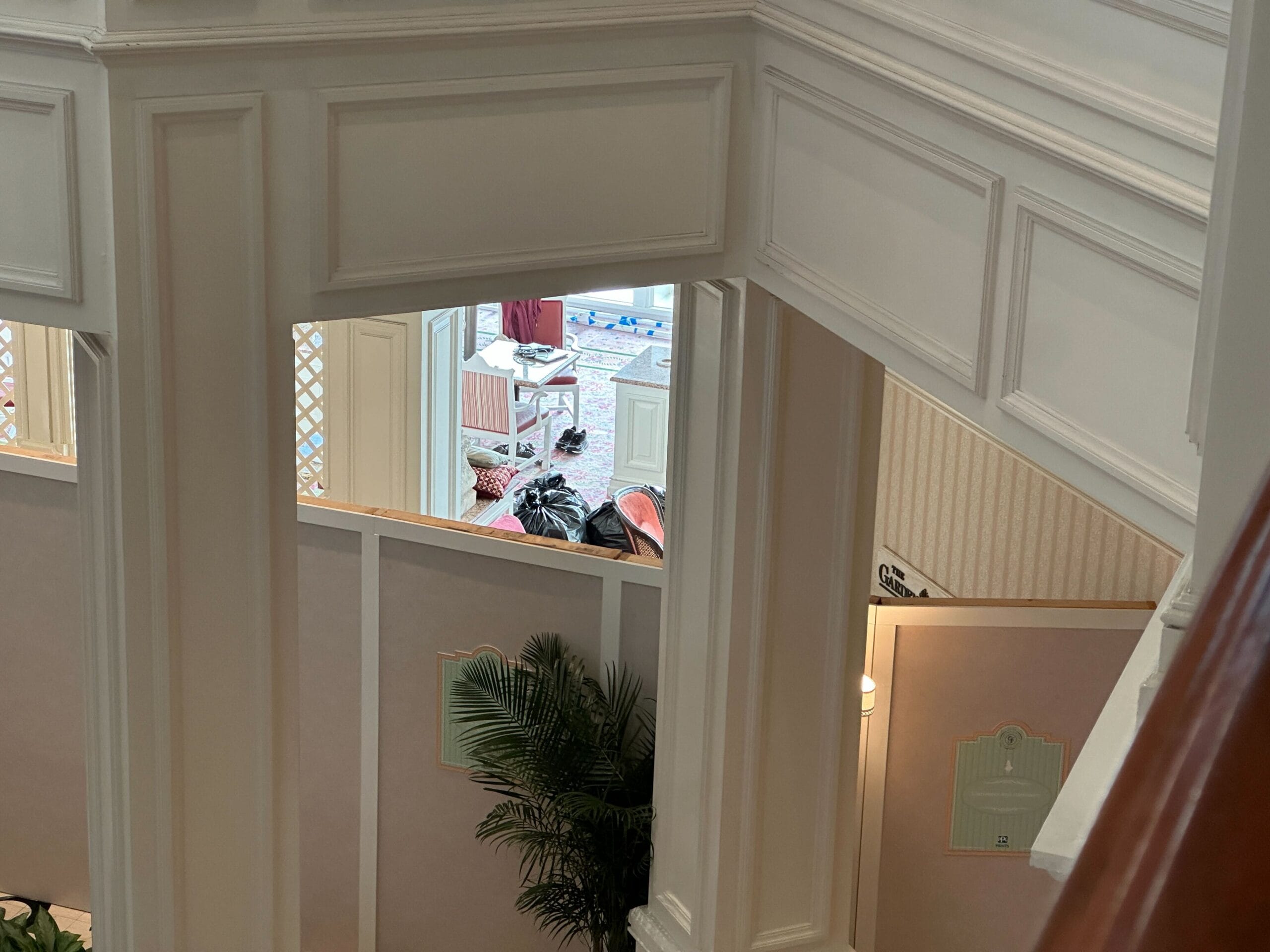 A person sits in a lobby area, viewed through white railings and walls inside a building with indoor plants.