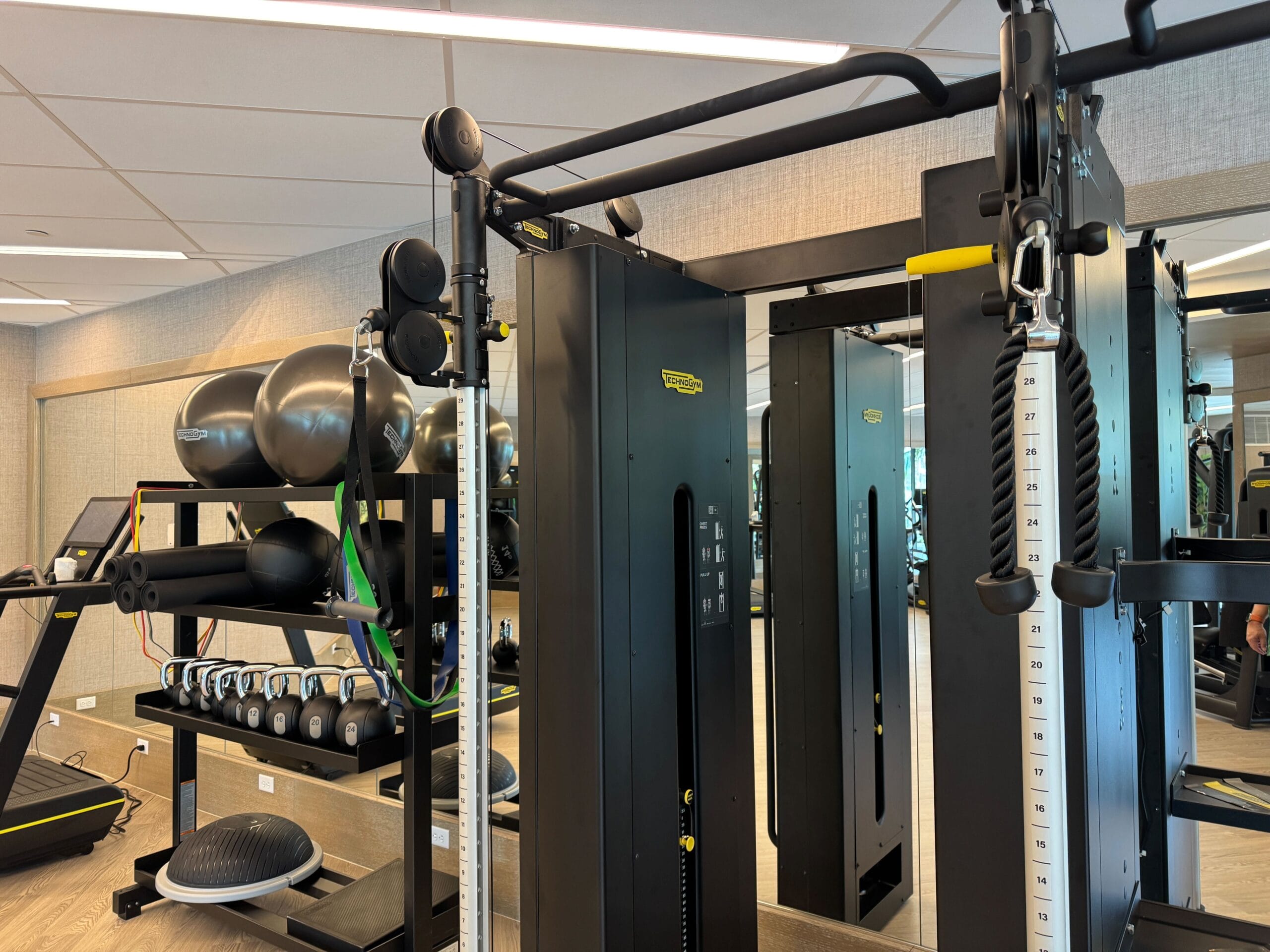 A gym with exercise equipment including a cable machine, dumbbells, resistance bands, exercise balls, and a treadmill.