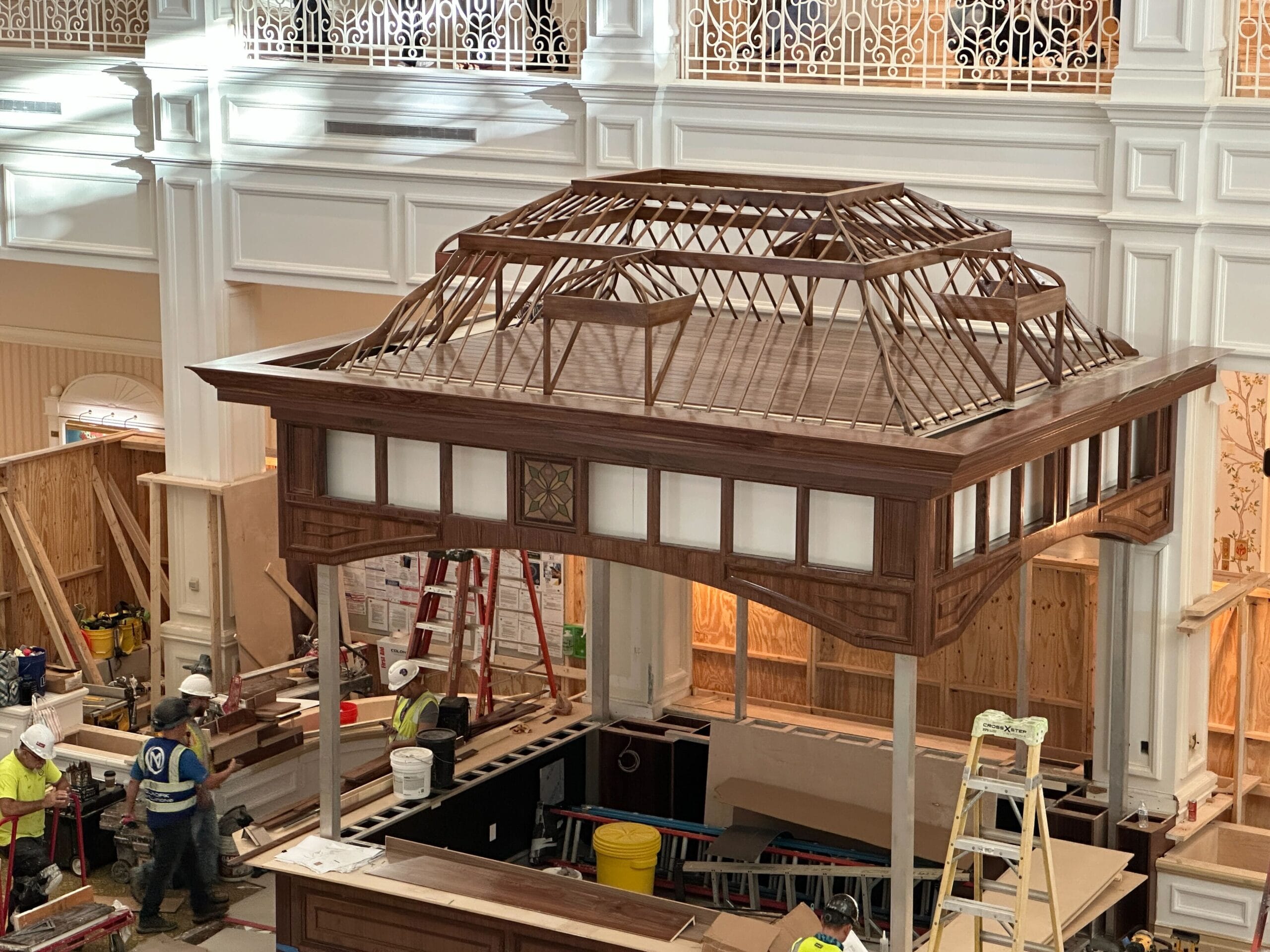 A wooden gazebo being built in Disney’s Grand Floridian Lobby, surrounded by workers and carpet rolls, evoking classic park elegance.