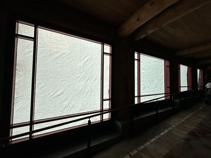 Large windows with opaque white coverings diffuse light in this dimly lit Wilderness Lodge interior with wooden beams.