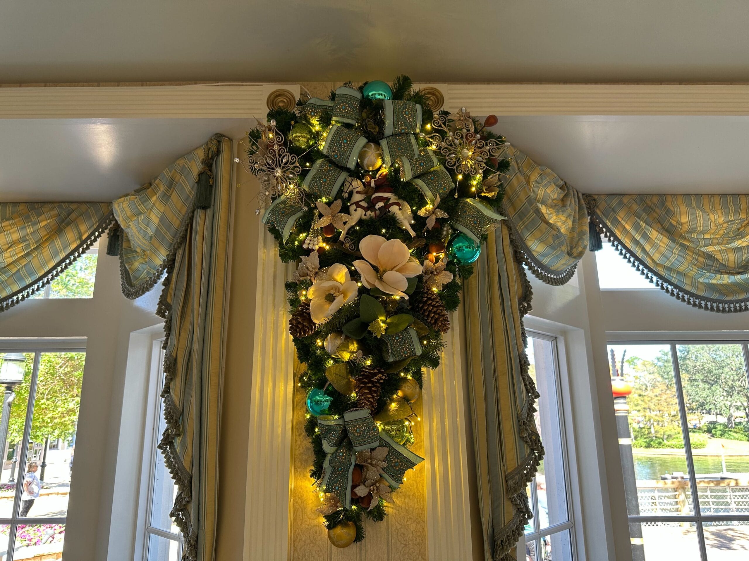 Elegant Christmas swag hanging on a wall, adorned with greenery, lights, blue and silver ornaments, magnolia flowers, and patterned ribbons.