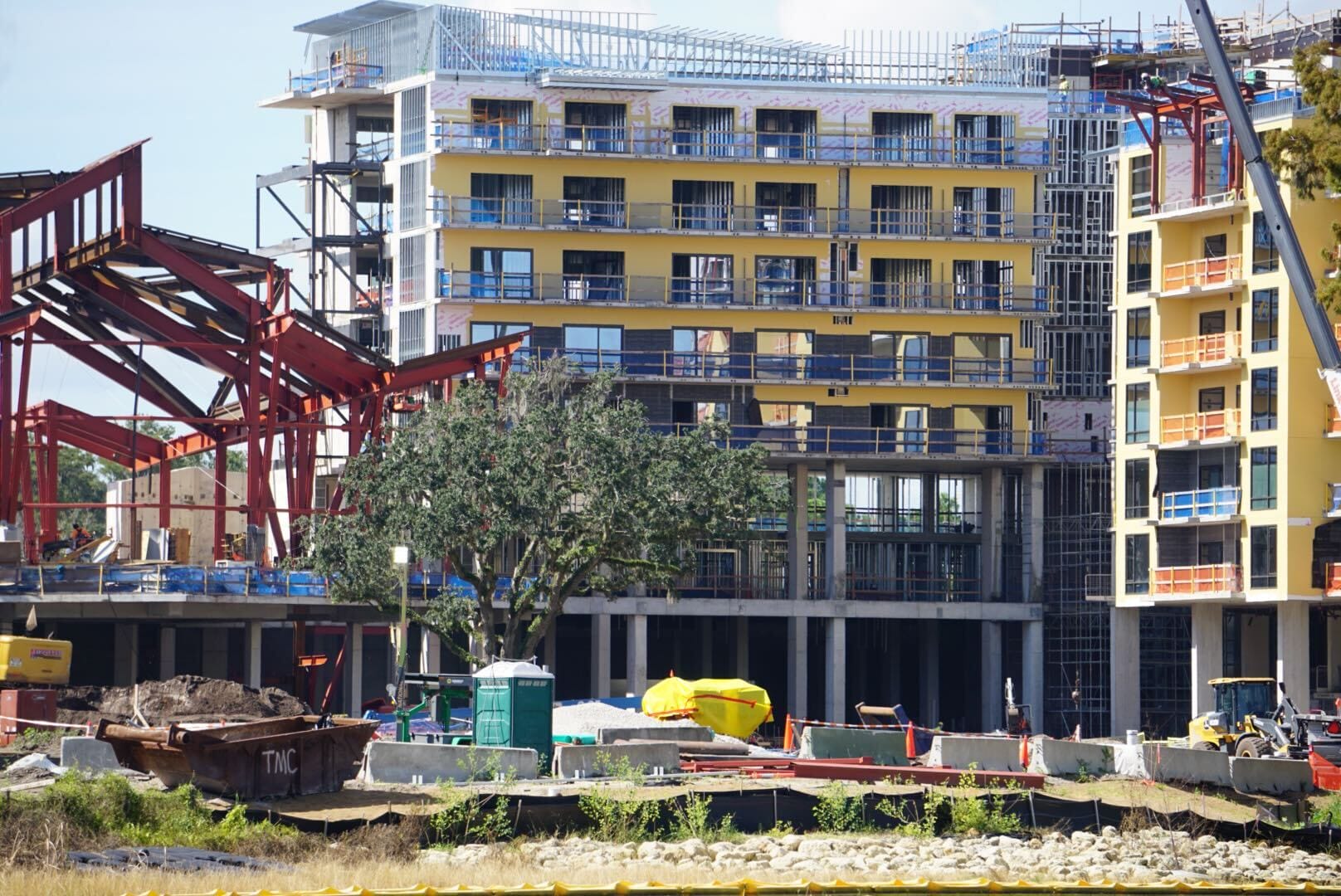 Construction site of Disney Lakeshore Lodge with a partially built yellow building, steel framework, and a tree in front.