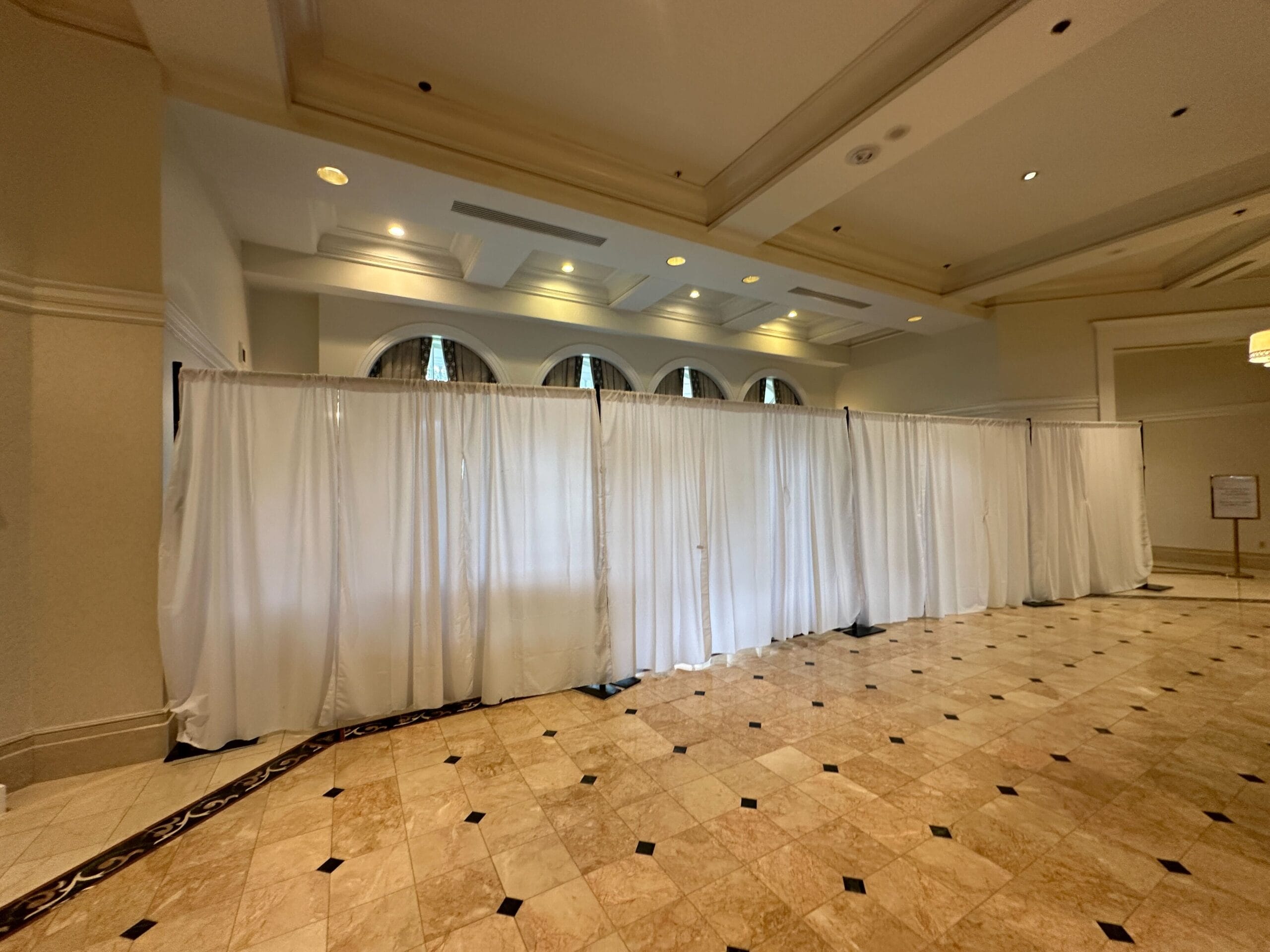 White divider curtains stretch across a tiled lobby with arched windows and recessed ceiling lights above.