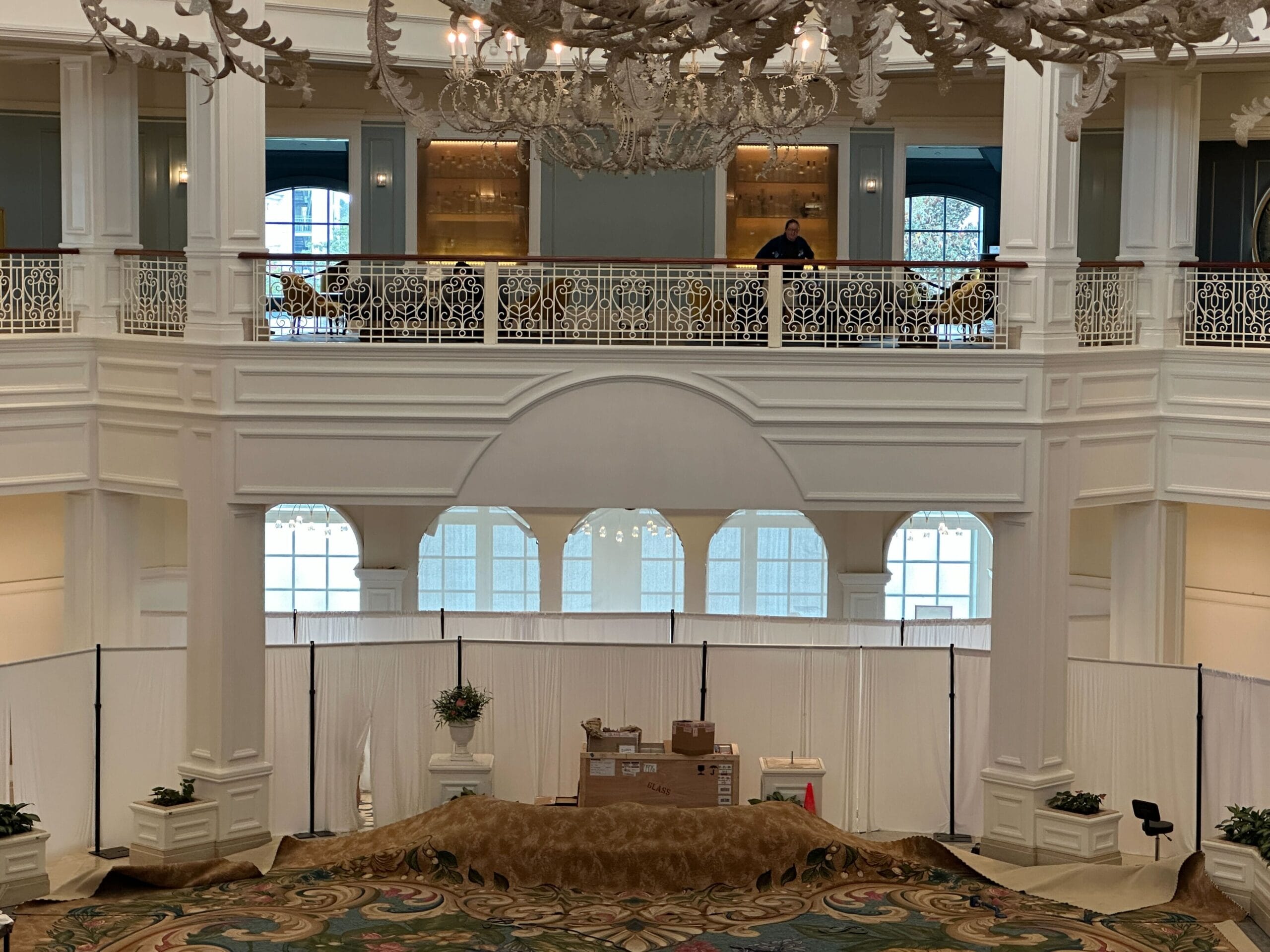A grand Grand Floridian Resort lobby at Walt Disney World, white railings, painting gear, and carpeting hidden behind white curtains.