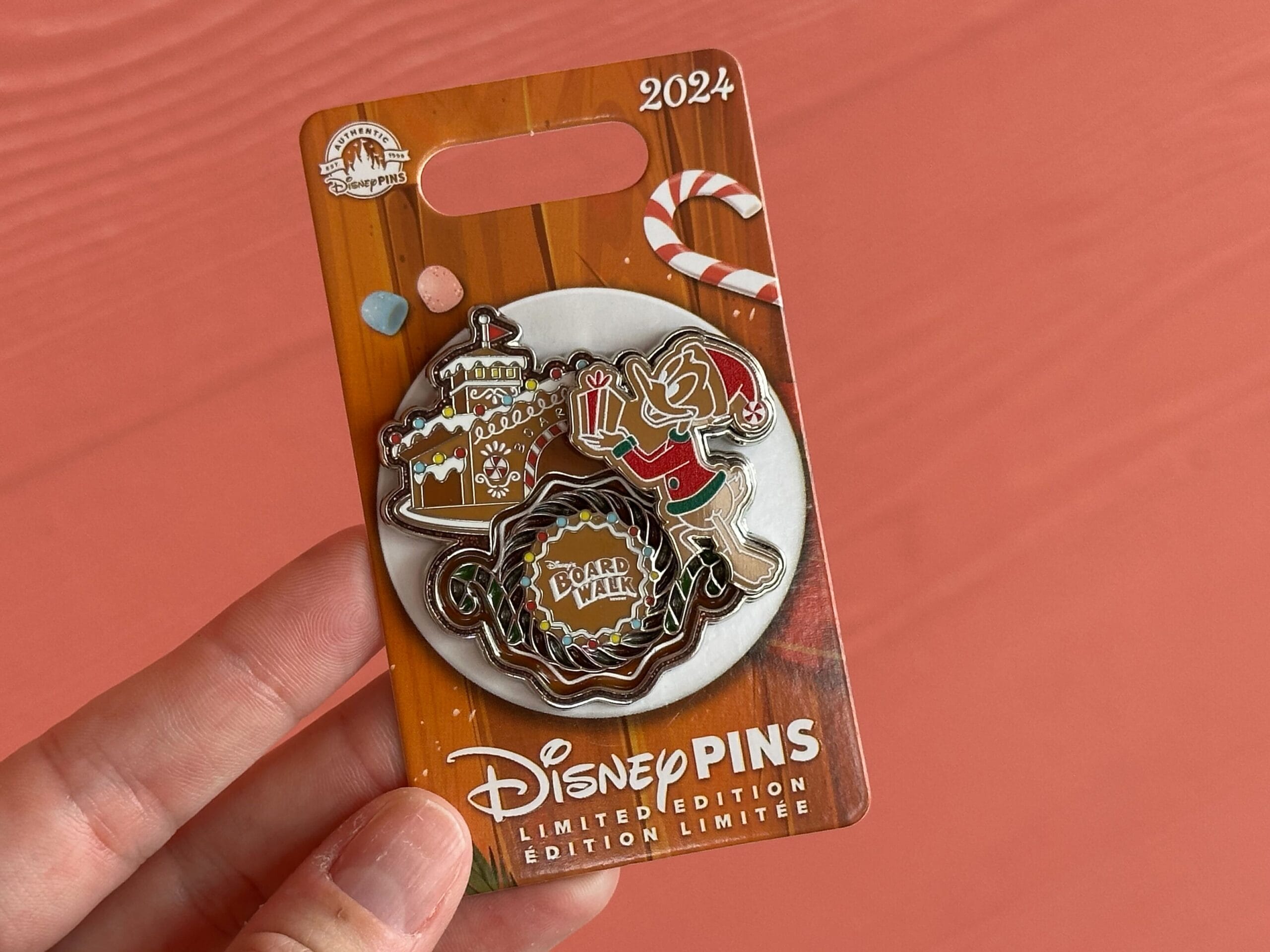 Hand holding a limited edition 2024 Disney pin featuring an elf, gingerbread house, and candy cane.