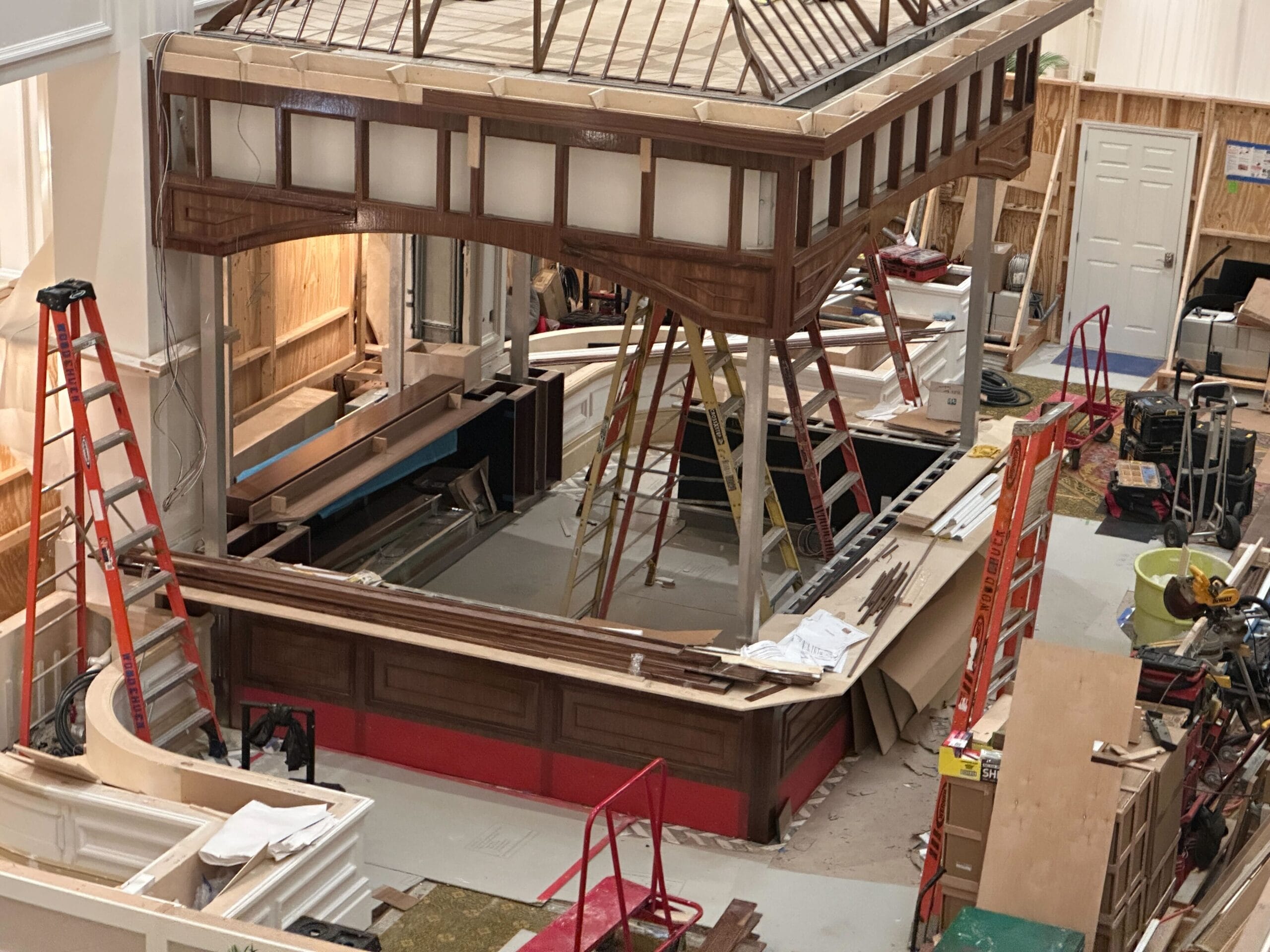 Indoor construction scene with ladders, tools, and a partially built wooden structure under a skylight.