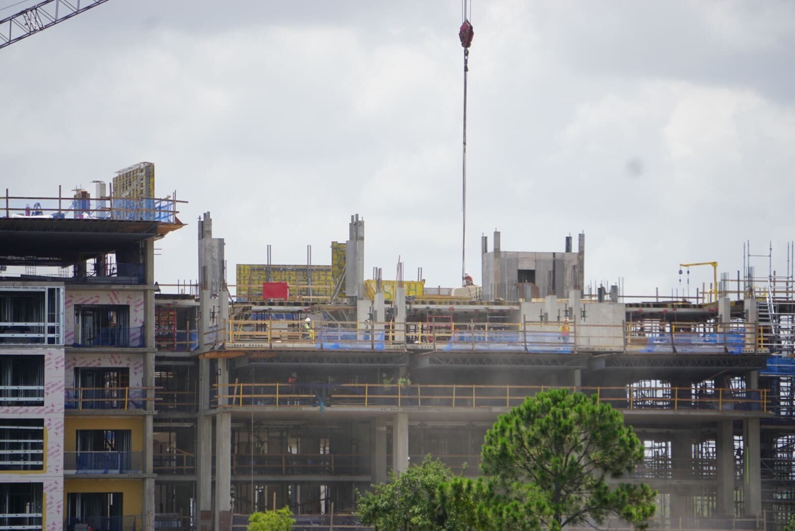 A multi-story building under construction with scaffolding, cranes, and cloudy sky in the background.