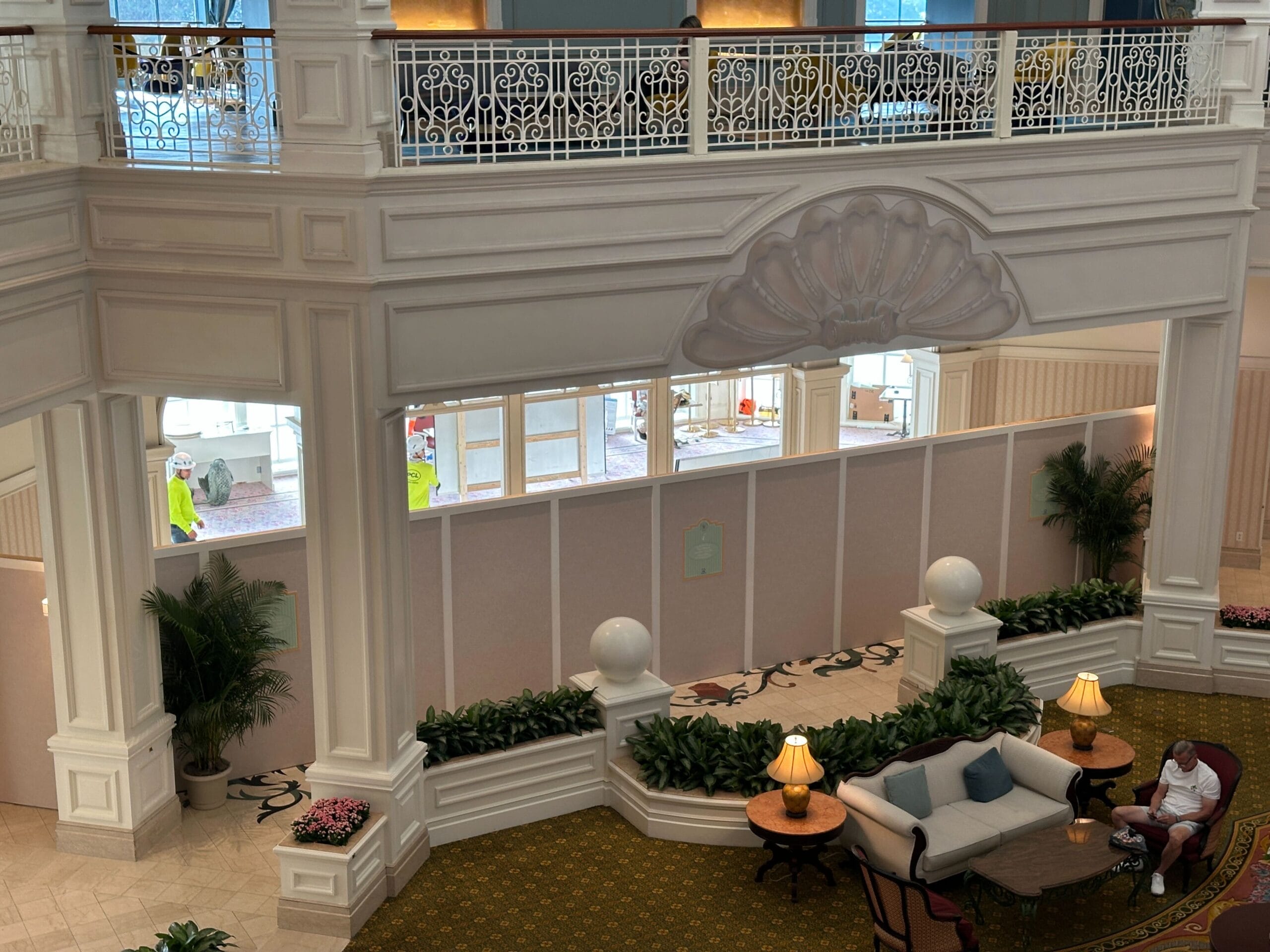 Hotel lobby with white railings, plants, h2o glow after hours food, cozy couches, and a person by a table with two lamps.