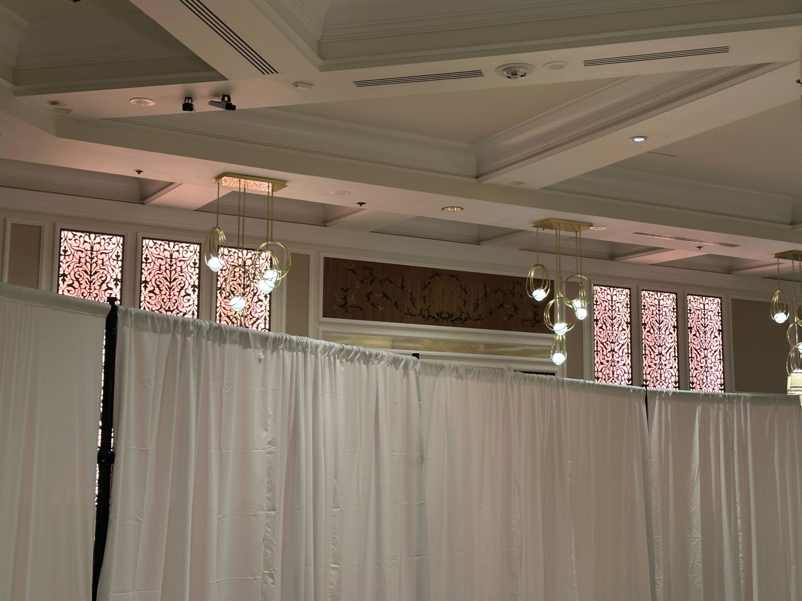 Ceiling with hanging lights and patterned windows above white partition curtains in an indoor space.