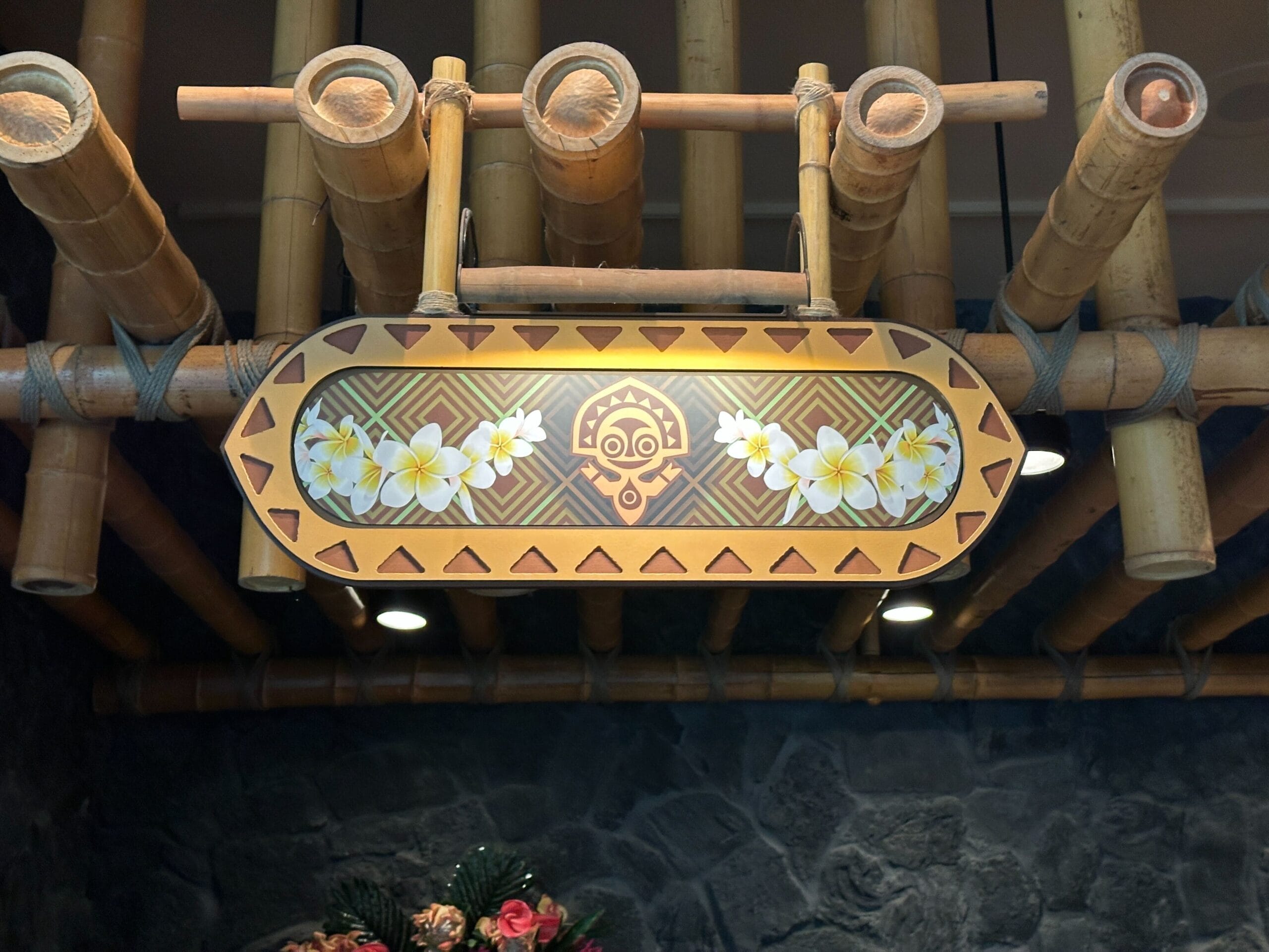 Wooden sign with tropical flowers and tribal design, like those at Disney's Polynesian Village Resort, hanging from bamboo poles.