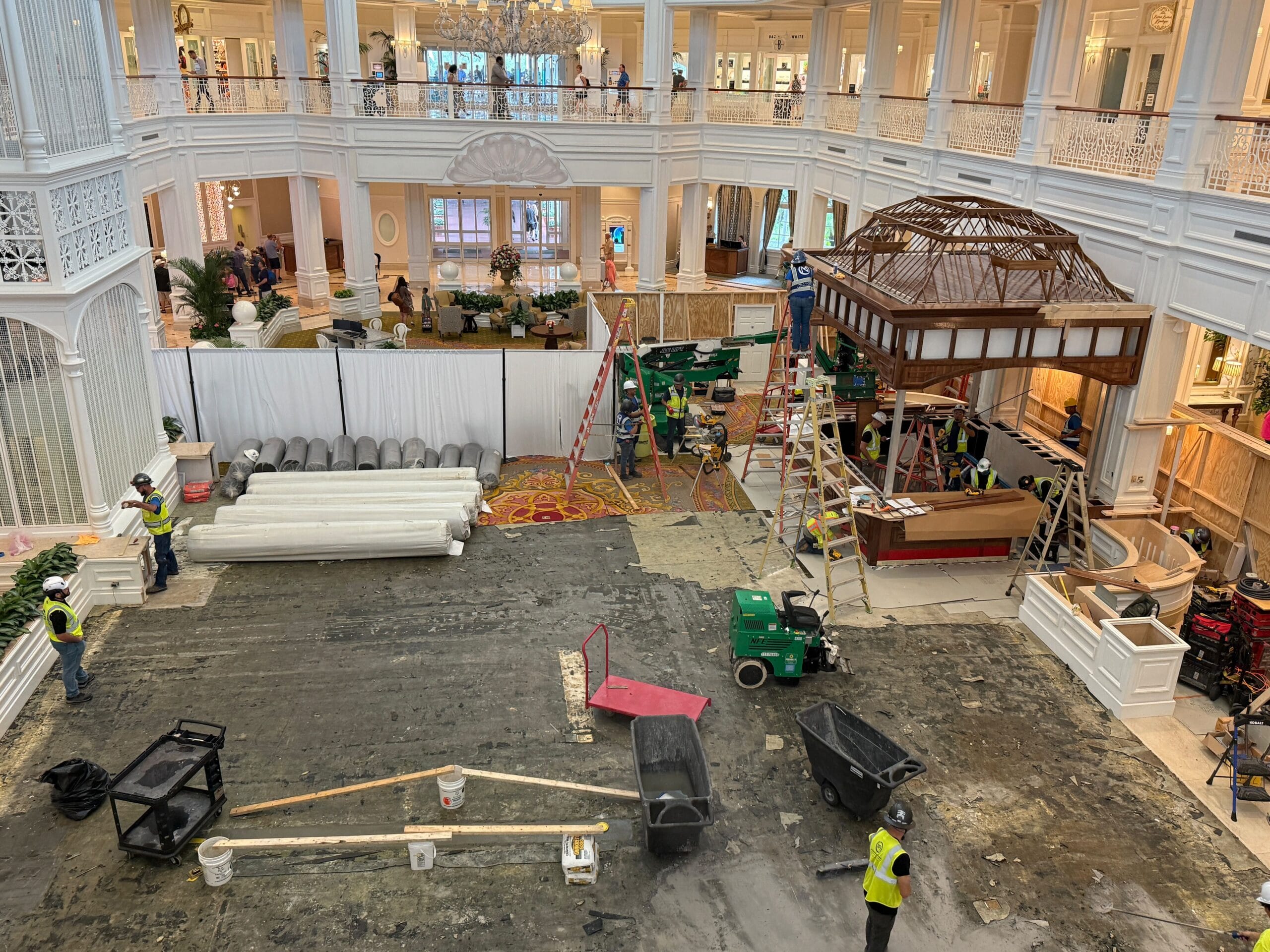Hotel lobby under renovation with workers, construction materials, and equipment on the ground floor, plastic covering floors.