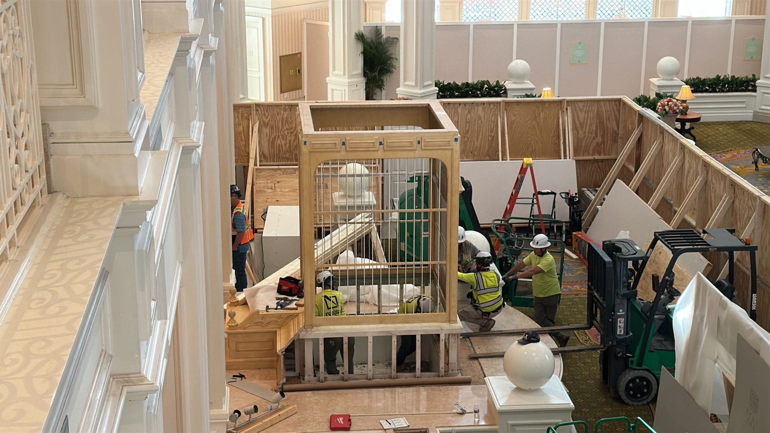 Construction workers assemble a large birdcage structure indoors during the Disney's Grand Floridian Resort lobby remodel.