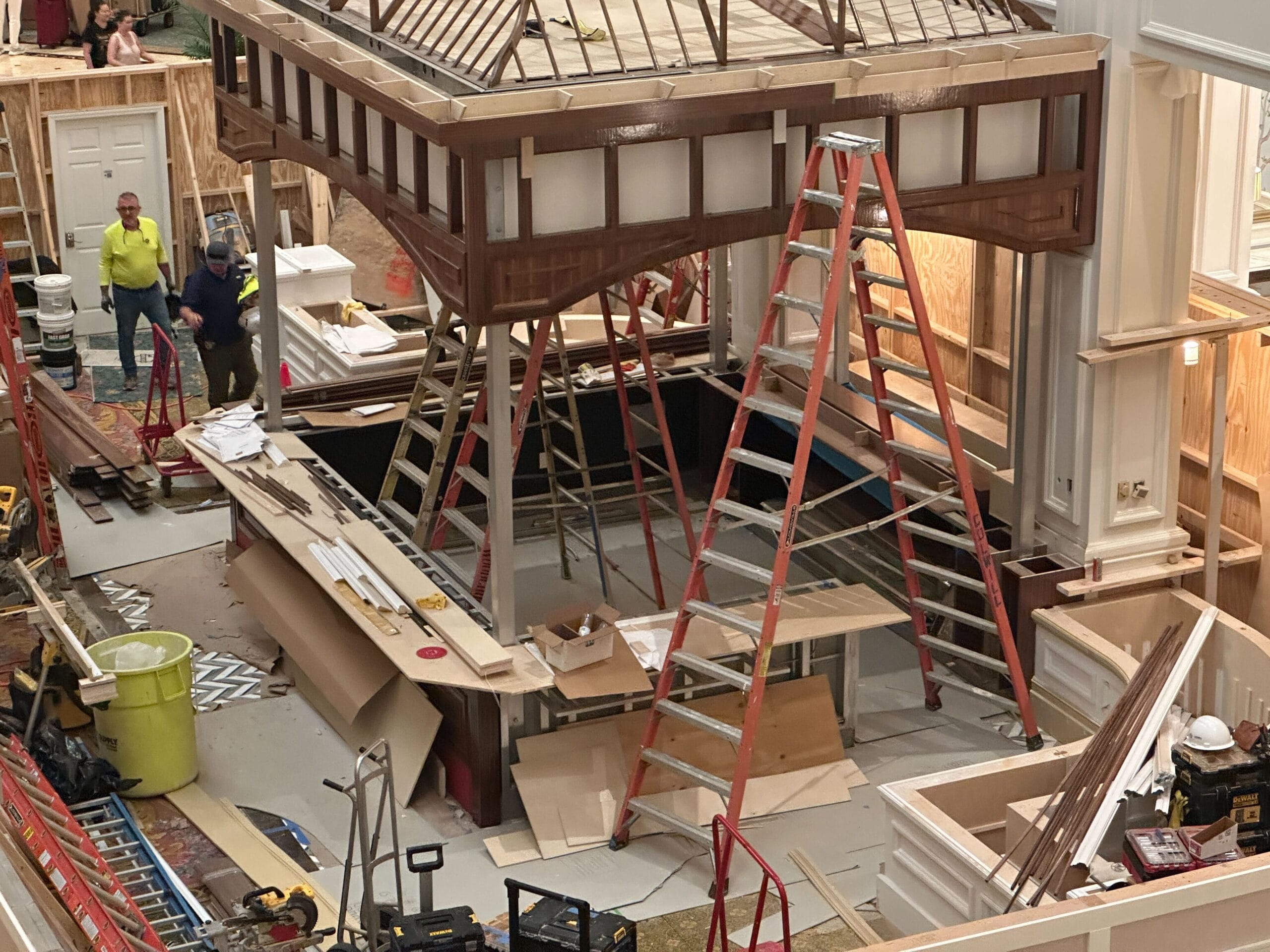 Several ladders and construction materials surround a partially built wooden structure inside a large room.
