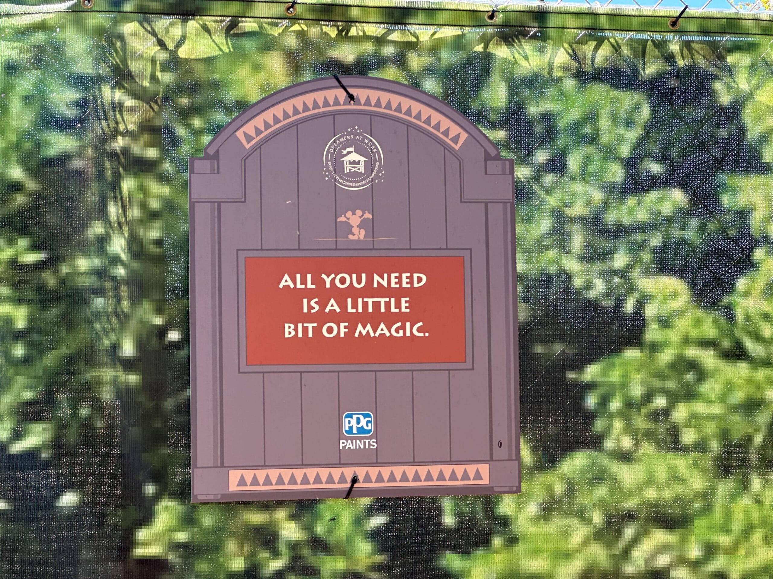A sign on a gate reads, All you need is a little bit of magic. The sign features the PPG Paints logo and is set against a background of green foliage.