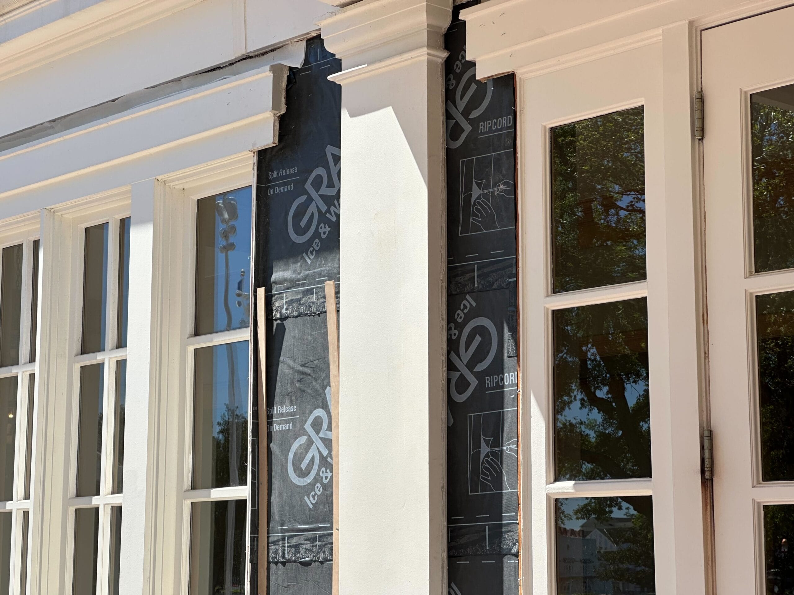 The building exterior at Disney's Yacht Club features white frames and exposed insulation cloaked by black wrap material near a column and window, reflecting ongoing construction efforts.
