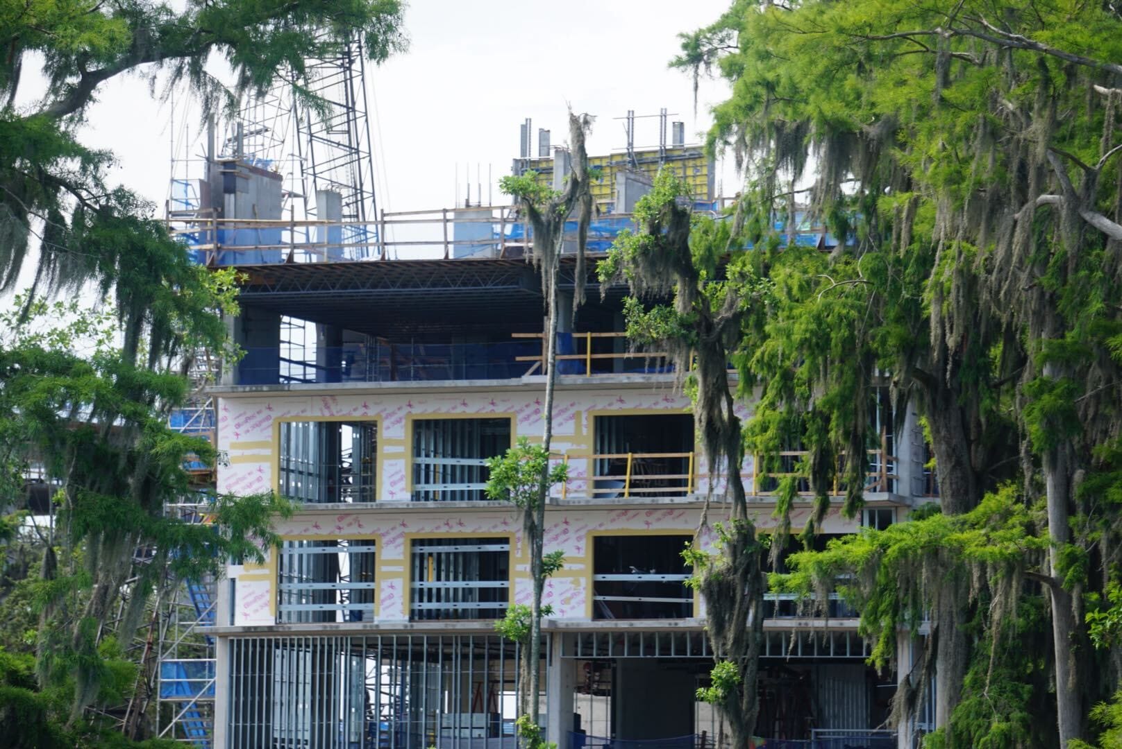 A multi-story building under construction surrounded by green trees and scaffolding.