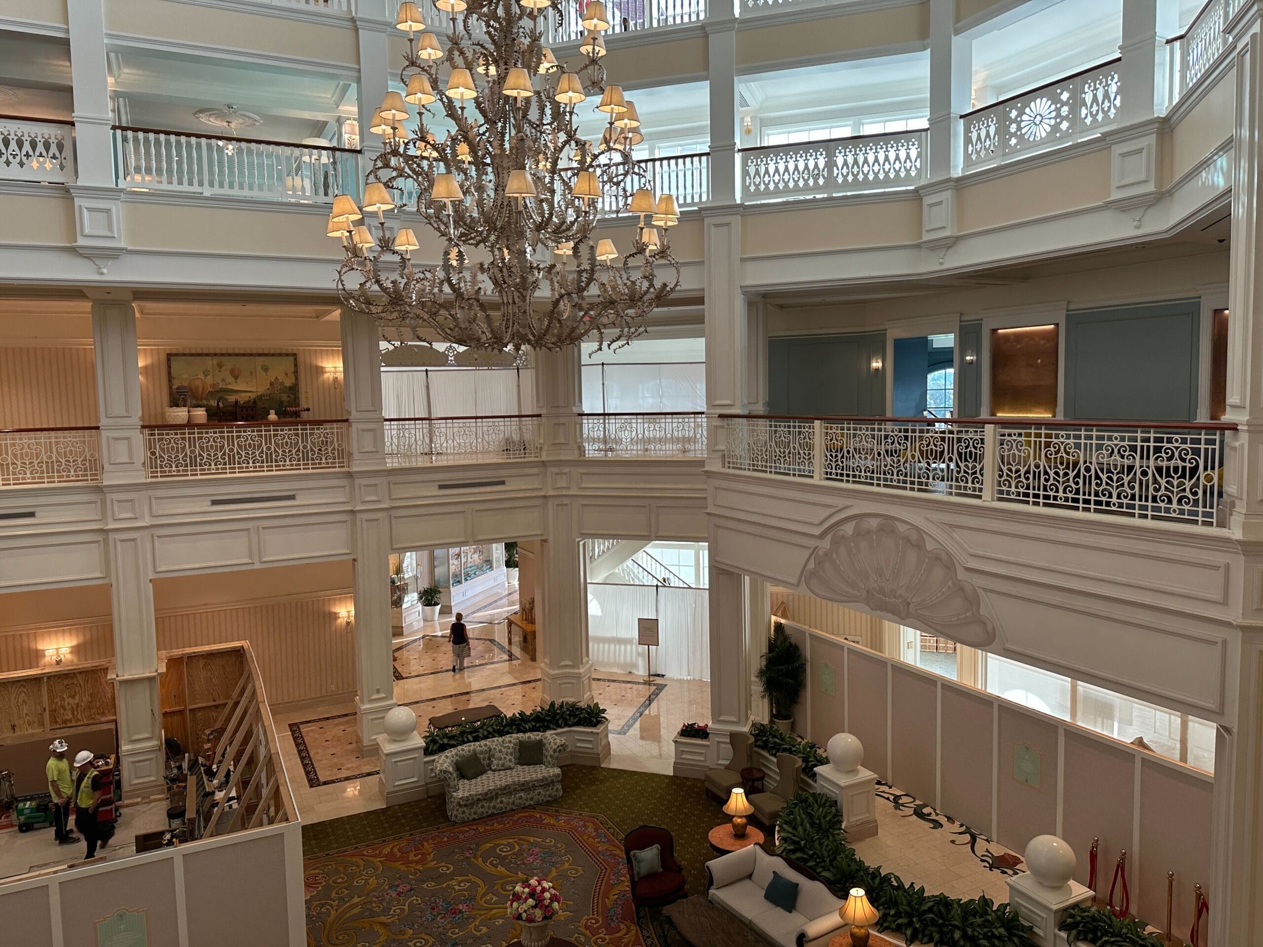 Elegant hotel lobby with a grand chandelier, large windows, and plush seating areas on patterned carpet.
