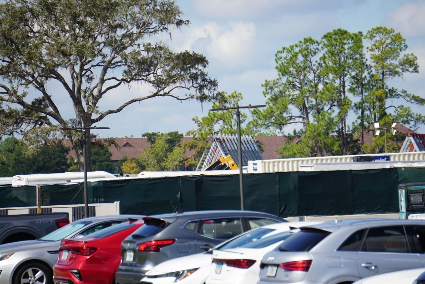 A parking lot with several cars near Disney Lakeshore Lodge, trees, and a partially cloudy sky in the background.