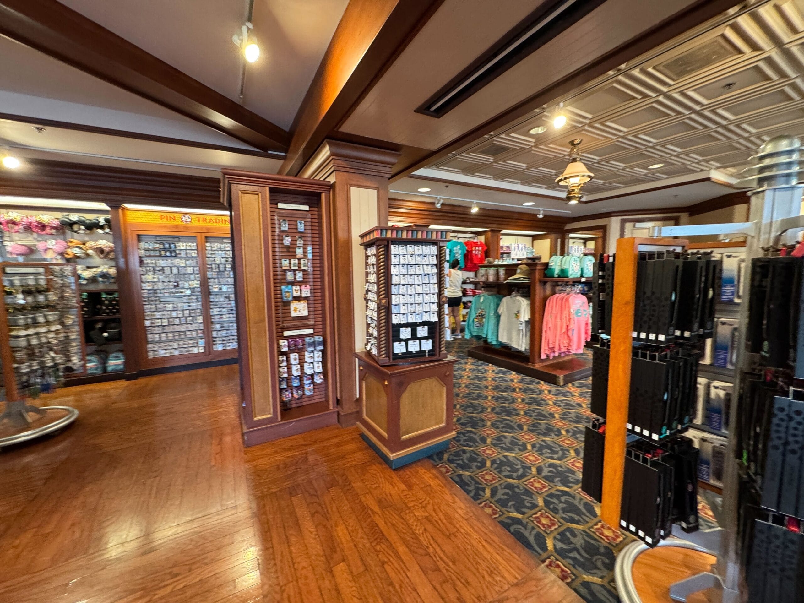 A retail store interior featuring display racks with various merchandise, including clothing, accessories, and souvenirs. Wooden flooring and overhead lighting are visible.
