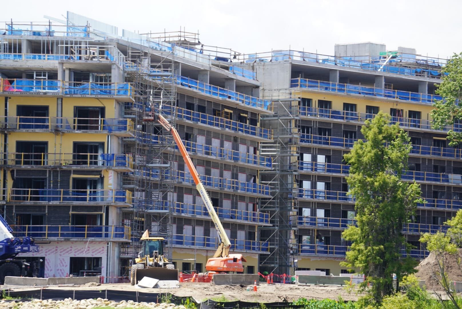 A multi-story building under construction with scaffolding, cranes, and workers visible on various levels.