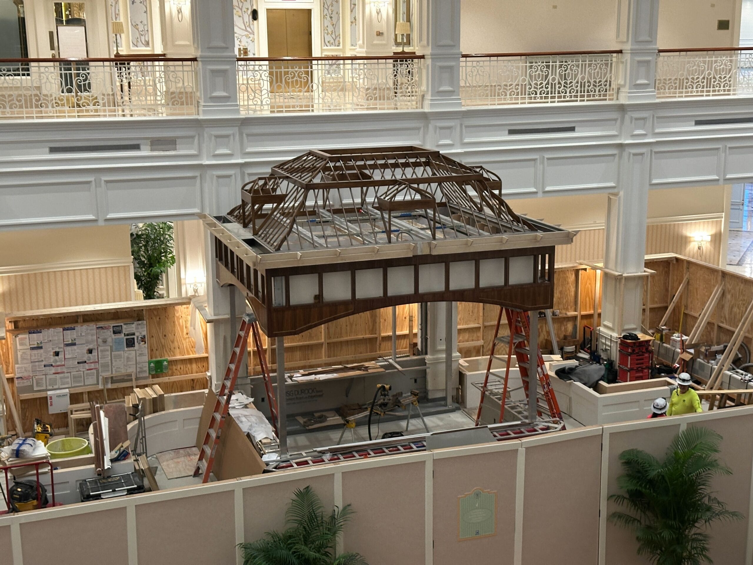 Indoor construction site at a Disney resort with wooden framework, ladders, and workers building a luxury hotel pavilion.