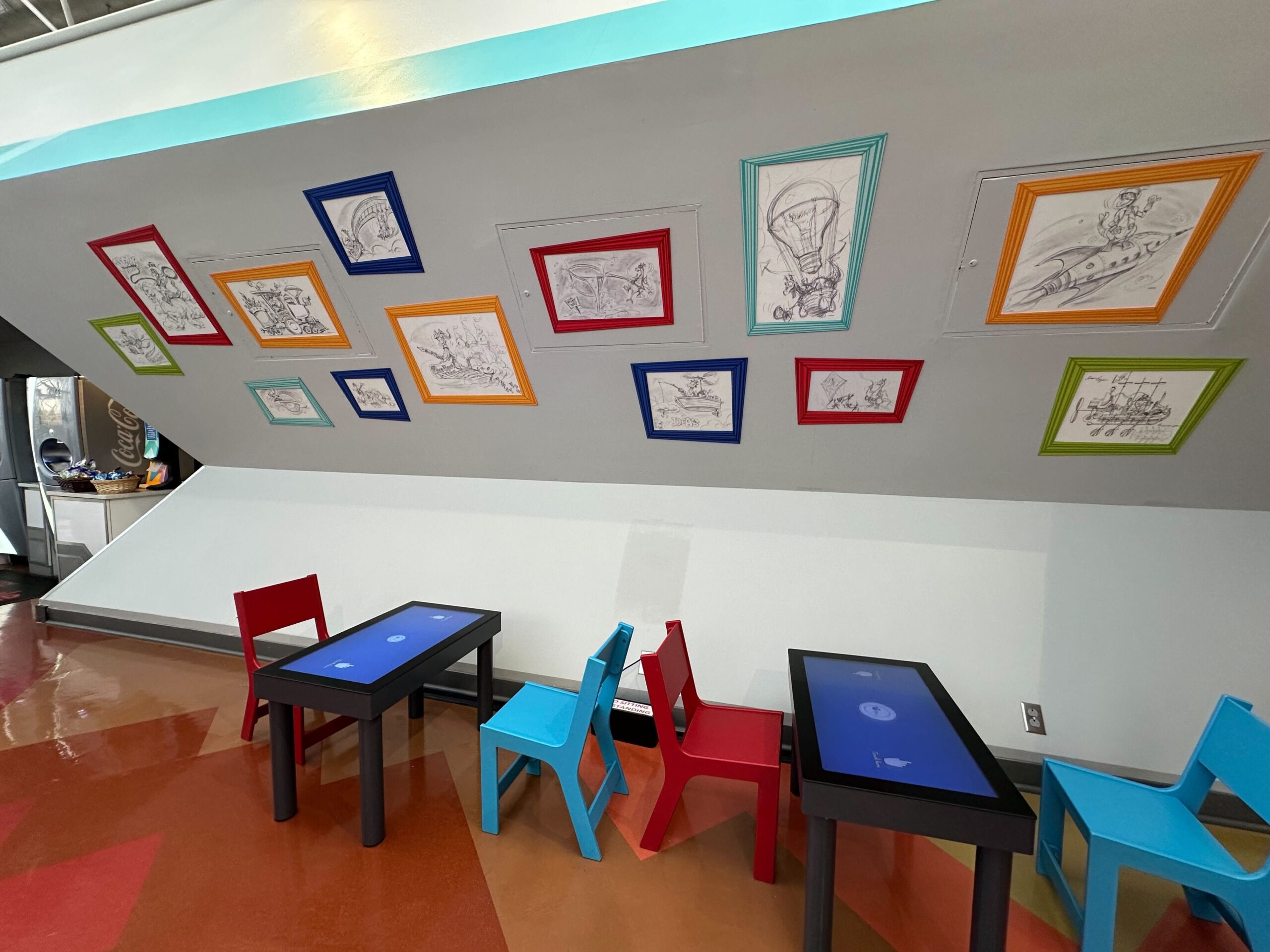 Children's area with small tables and chairs, under a sloped ceiling decorated with framed sketches. Children's area with small tables and chairs, under a sloped ceiling decorated with framed sketches.
