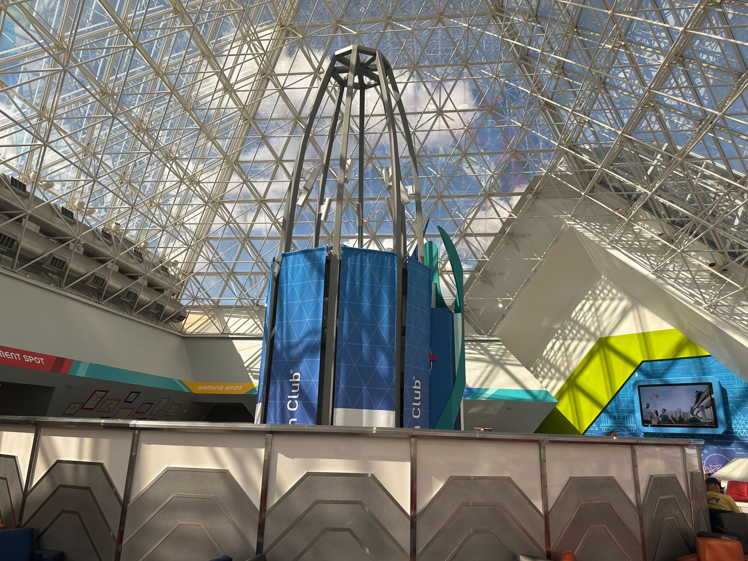 A geometric structure with a metal frame and blue panels stands inside a glass-domed building, surrounded by angular walls and lit by natural light. A geometric structure with a metal frame and blue panels stands inside a glass-domed building, surrounded by angular walls and lit by natural light.