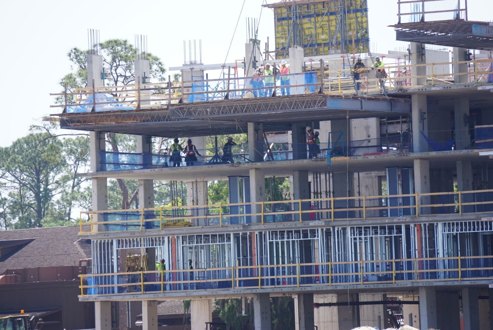 Nestled amid the trees, the construction site of a multi-story building resembles a bustling lakeshore lodge, with workers strategically positioned across various levels and surrounded by scaffolding and metal framework. Nestled amid the trees, the construction site of a multi-story building resembles a bustling lakeshore lodge, with workers strategically positioned across various levels and surrounded by scaffolding and metal framework.