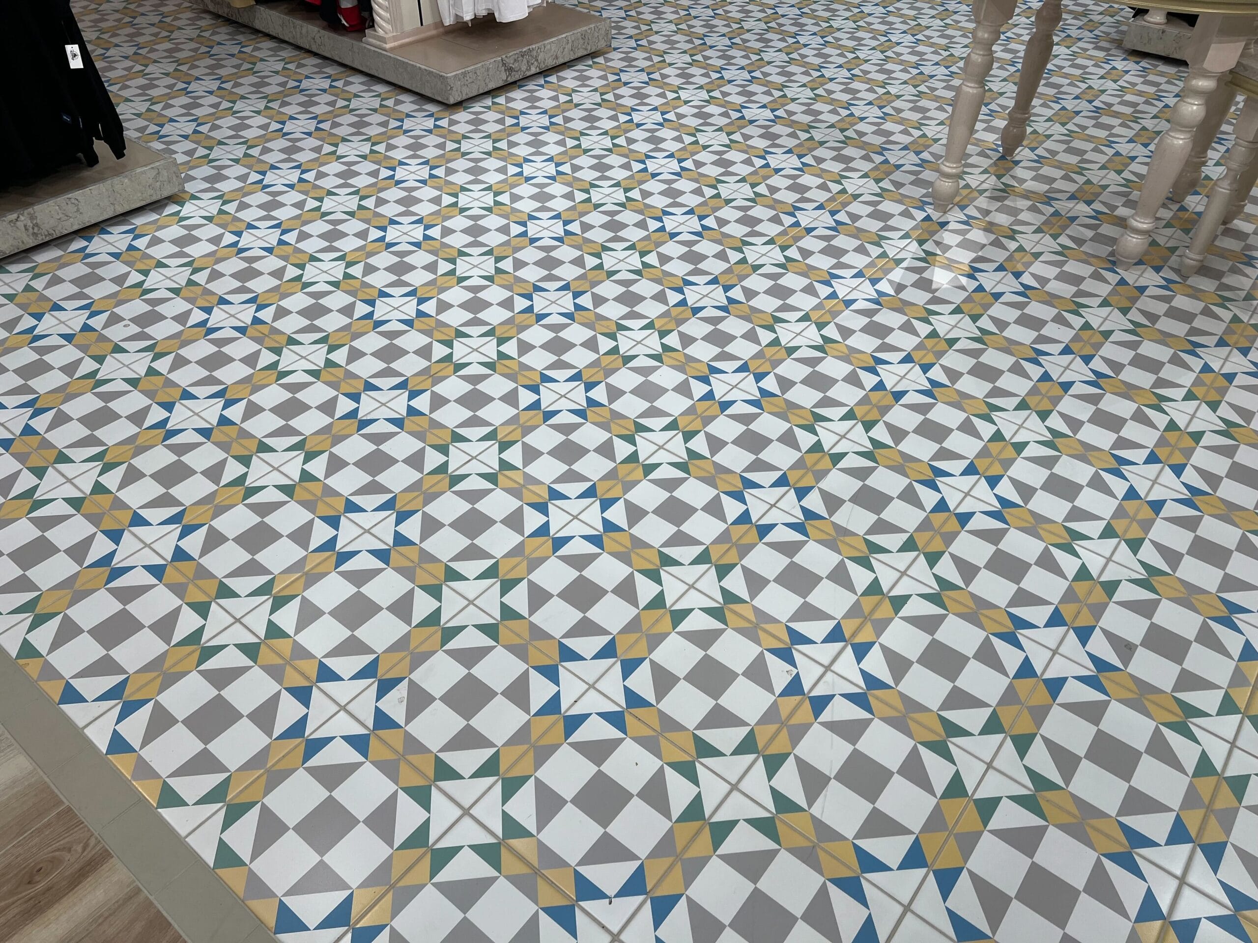 Colorful geometric tile floor—blue, green, yellow diamond patterns—at Thimbles & Threads. Furniture legs are visible. Colorful geometric tile floor—blue, green, yellow diamond patterns—at Thimbles & Threads. Furniture legs are visible.