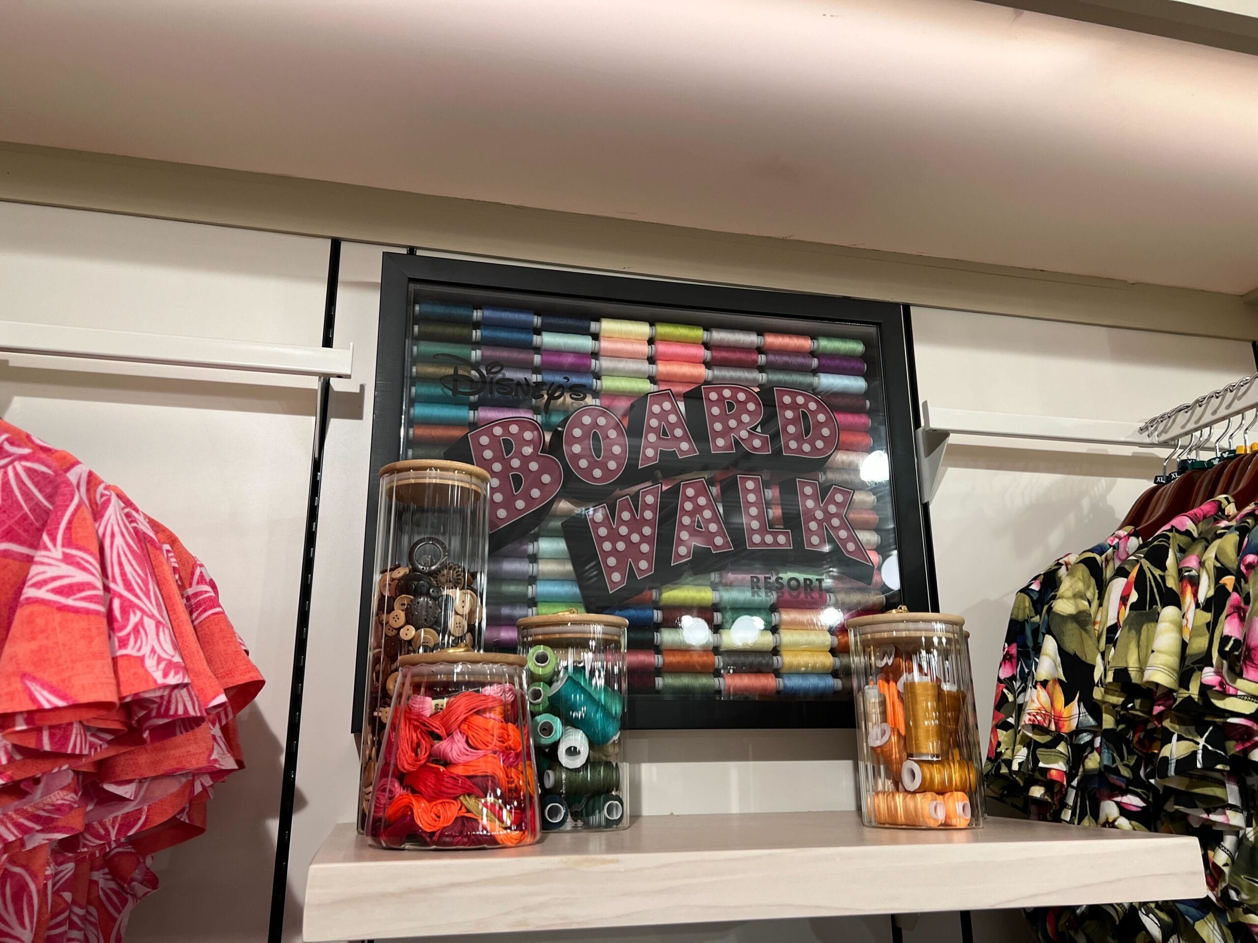 Framed Boardwalk sign at Thimbles & Threads with colorful spools, jars, and tropical shirts on display. Framed Boardwalk sign at Thimbles & Threads with colorful spools, jars, and tropical shirts on display.