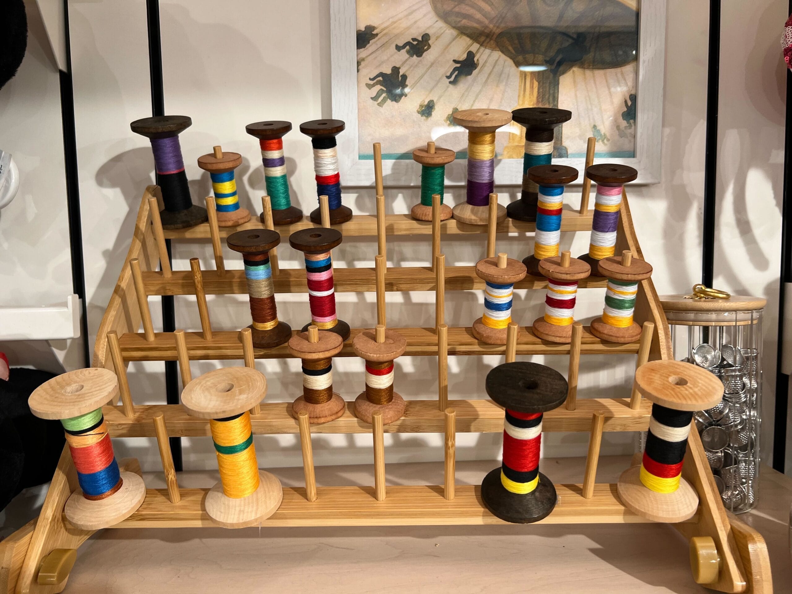 Wooden rack of colorful thread spools from Thimbles & Threads; framed picture hangs behind at Screen Door General Store. Wooden rack of colorful thread spools from Thimbles & Threads; framed picture hangs behind at Screen Door General Store.