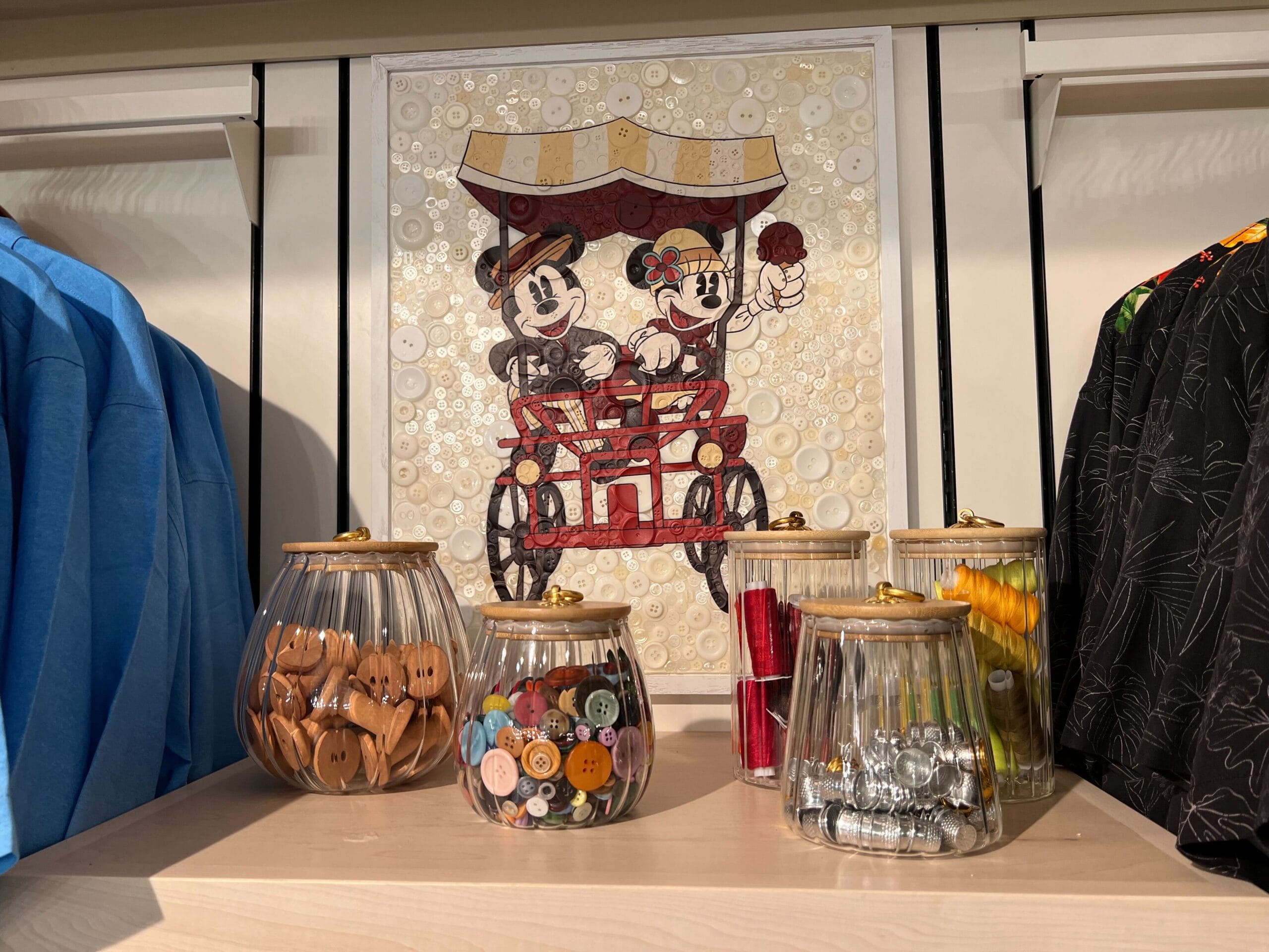 Jars of buttons and sewing supplies from Thimbles & Threads sit below a picture of Mickey and Minnie Mouse riding a bicycle. Jars of buttons and sewing supplies from Thimbles & Threads sit below a picture of Mickey and Minnie Mouse riding a bicycle.