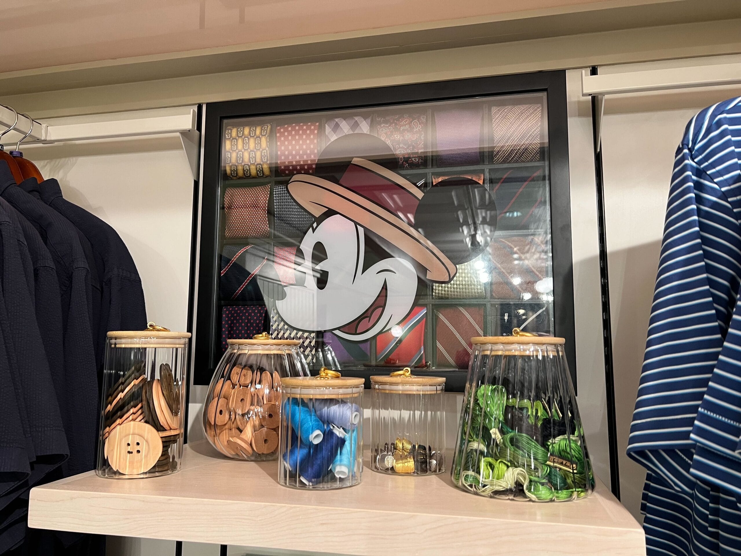 Jars of buttons and sewing notions from Thimbles & Threads on a shelf, with Mickey Mouse pictured behind them. Jars of buttons and sewing notions from Thimbles & Threads on a shelf, with Mickey Mouse pictured behind them.