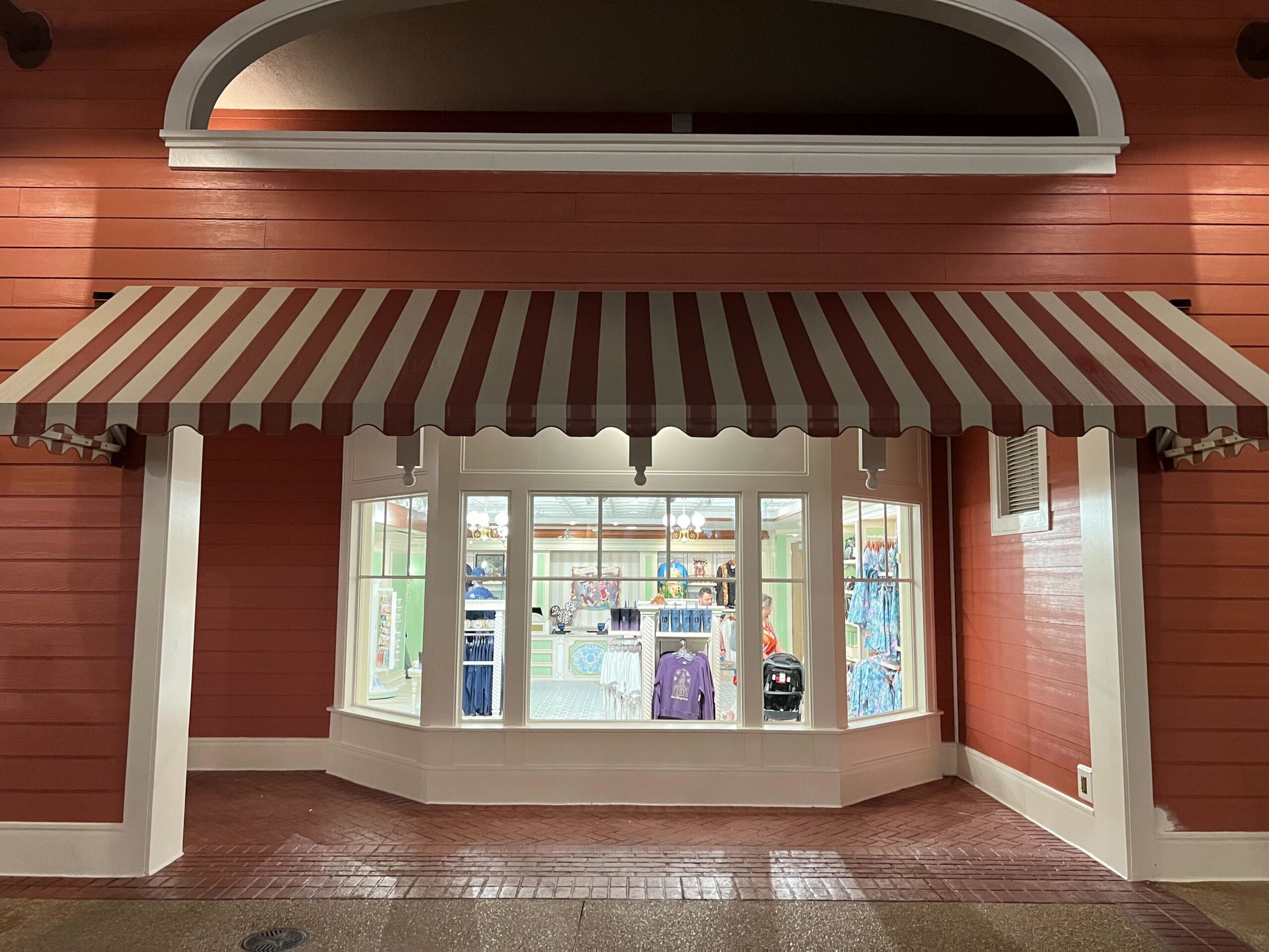 A red building with a striped awning, home to Thimbles & Threads, displays gifts and clothes in its brightly lit shop window. A red building with a striped awning, home to Thimbles & Threads, displays gifts and clothes in its brightly lit shop window.