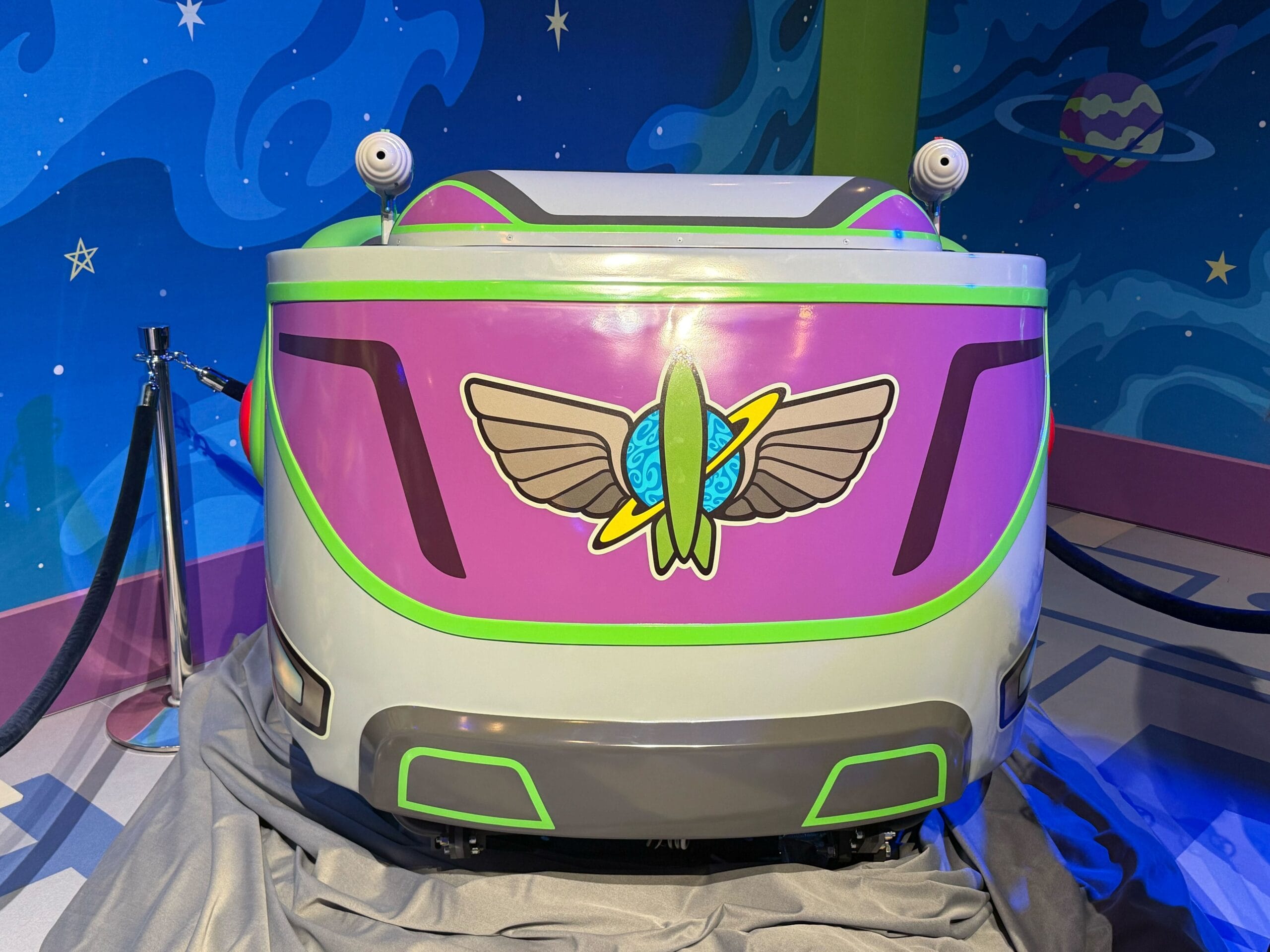 First look at colorful Buzz Lightyear Space Ranger Spin ride vehicle with rocket emblem, set in a cosmic planet-filled backdrop. First look at colorful Buzz Lightyear Space Ranger Spin ride vehicle with rocket emblem, set in a cosmic planet-filled backdrop.