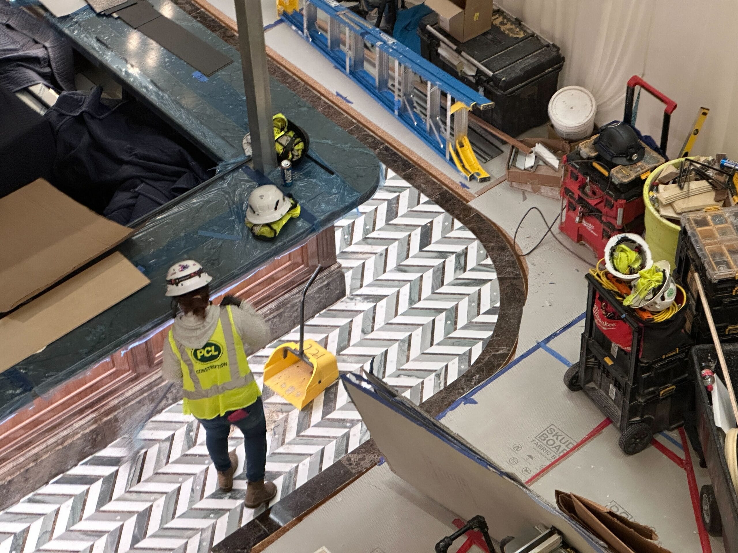 Construction worker sweeping detailed floor at Grand Floridian, tools and helmets nearby; shelving installed—no Disney castle in view. Construction worker sweeping detailed floor at Grand Floridian, tools and helmets nearby; shelving installed—no Disney castle in view.
