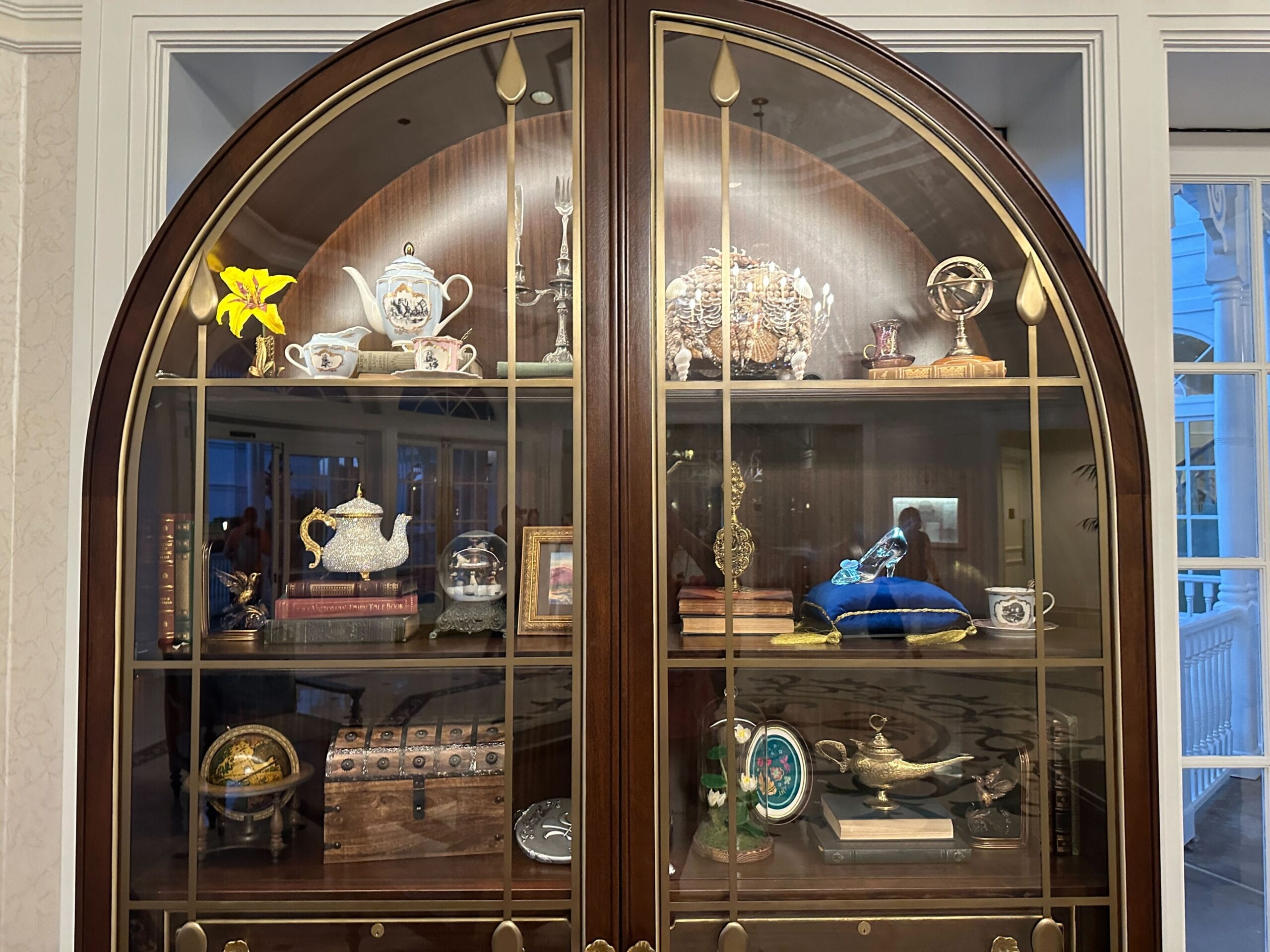 An arched dark wood cabinet with a glass front in the Grand Floridian lobby bar showcases homages to classic Disney films. An arched dark wood cabinet with a glass front in the Grand Floridian lobby bar showcases homages to classic Disney films.