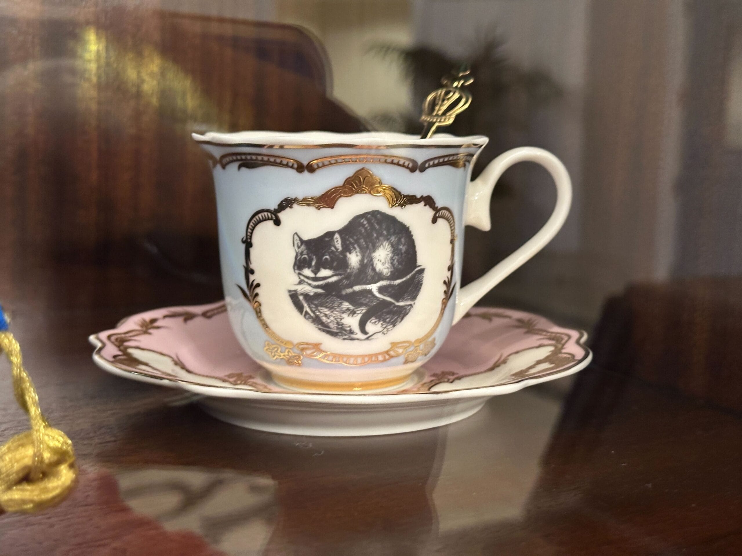 A teacup with a grinning cat design and gold accents on a saucer in a glass-front display case in the refurbished Grand Floridian lobby bar. A teacup with a grinning cat design and gold accents on a saucer in a glass-front display case in the refurbished Grand Floridian lobby bar.