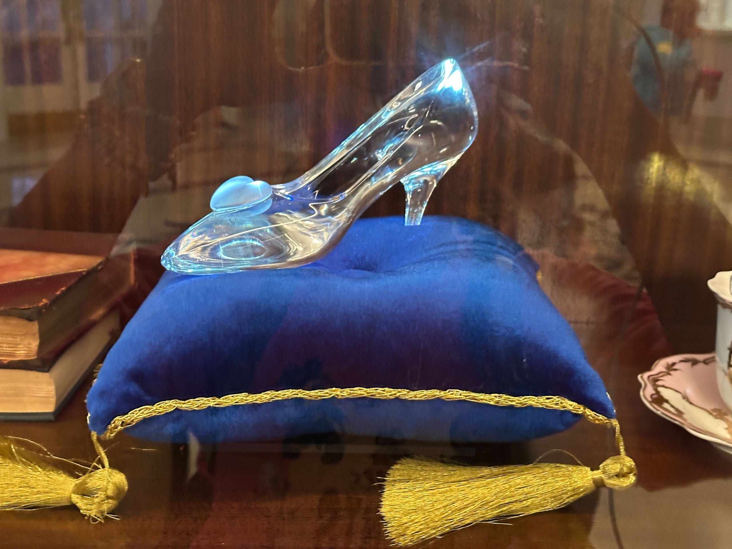 A sparkling glass slipper on a royal blue cushion with yellow trim in a glass-front display case in the refurbished Grand Floridian lobby bar. A sparkling glass slipper on a royal blue cushion with yellow trim in a glass-front display case in the refurbished Grand Floridian lobby bar.