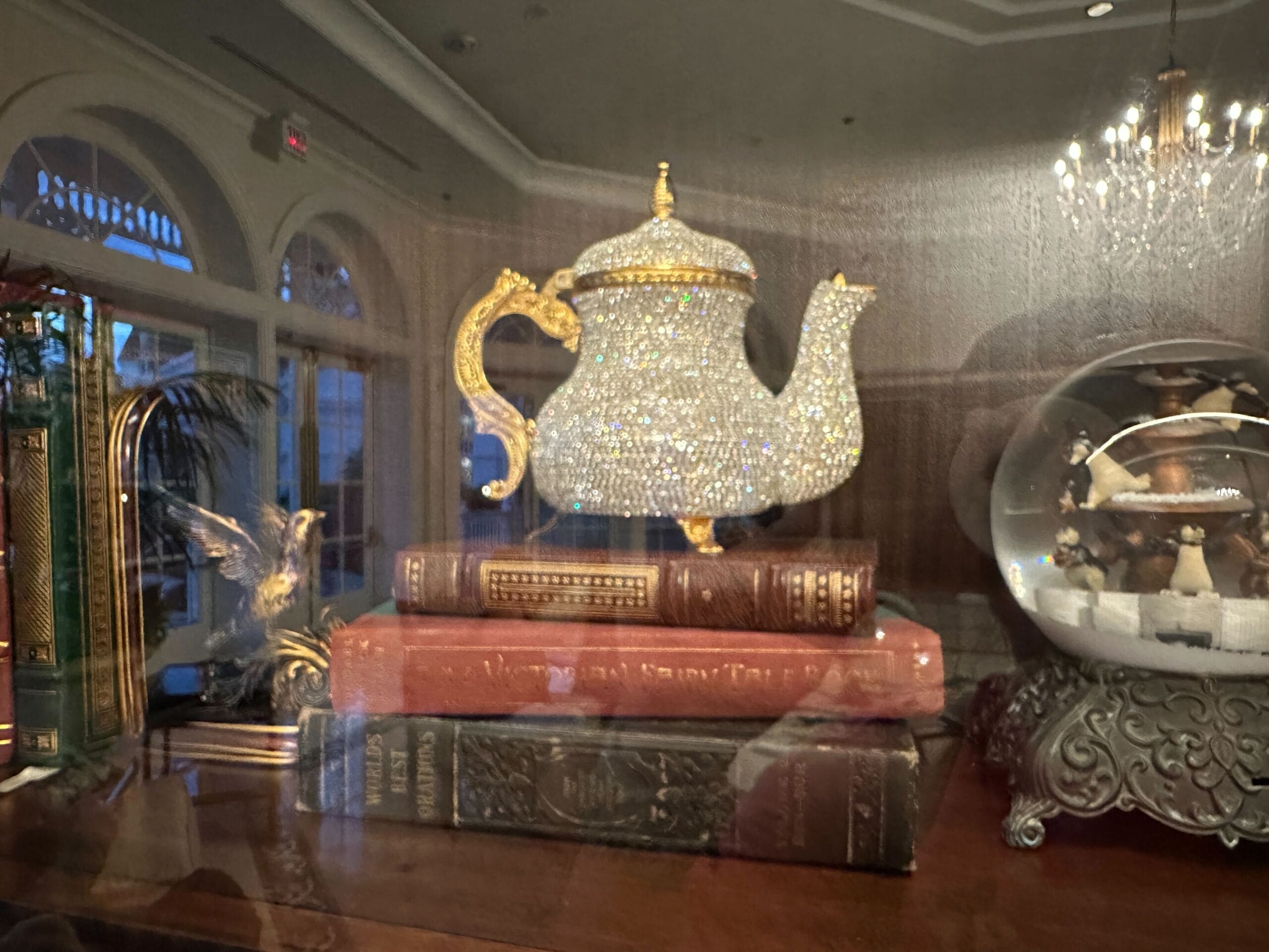 A crystal teapot with gold accents sits atop three vintage books next to a snow globe in a glass-front display case in the refurbished Grand Floridian lobby bar. A crystal teapot with gold accents sits atop three vintage books next to a snow globe in a glass-front display case in the refurbished Grand Floridian lobby bar.