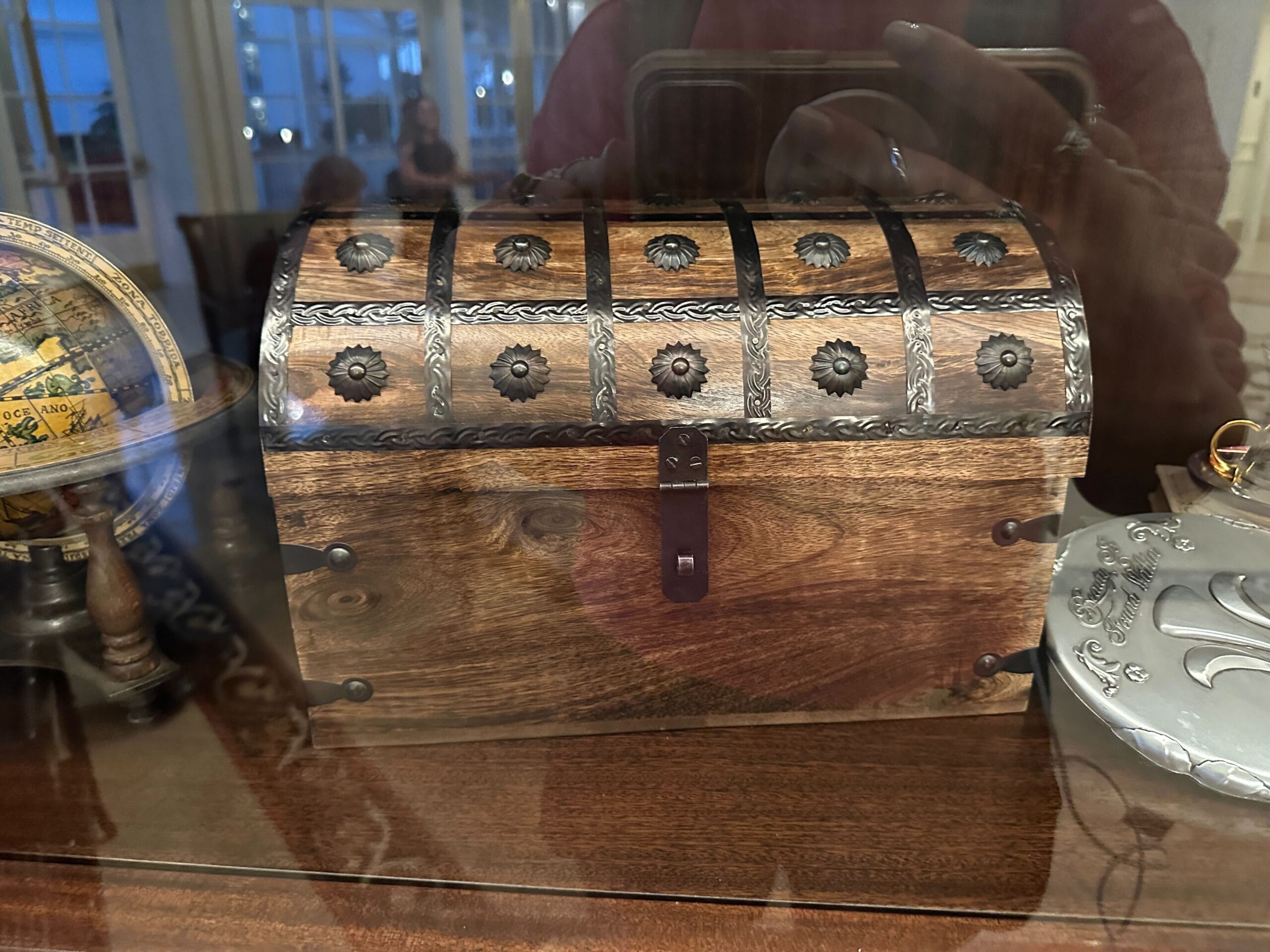 A wooden treasure chest with metal accents sits on a warmly lit shelf in a glass-front display case in the refurbished Grand Floridian lobby bar. A wooden treasure chest with metal accents sits on a warmly lit shelf in a glass-front display case in the refurbished Grand Floridian lobby bar.