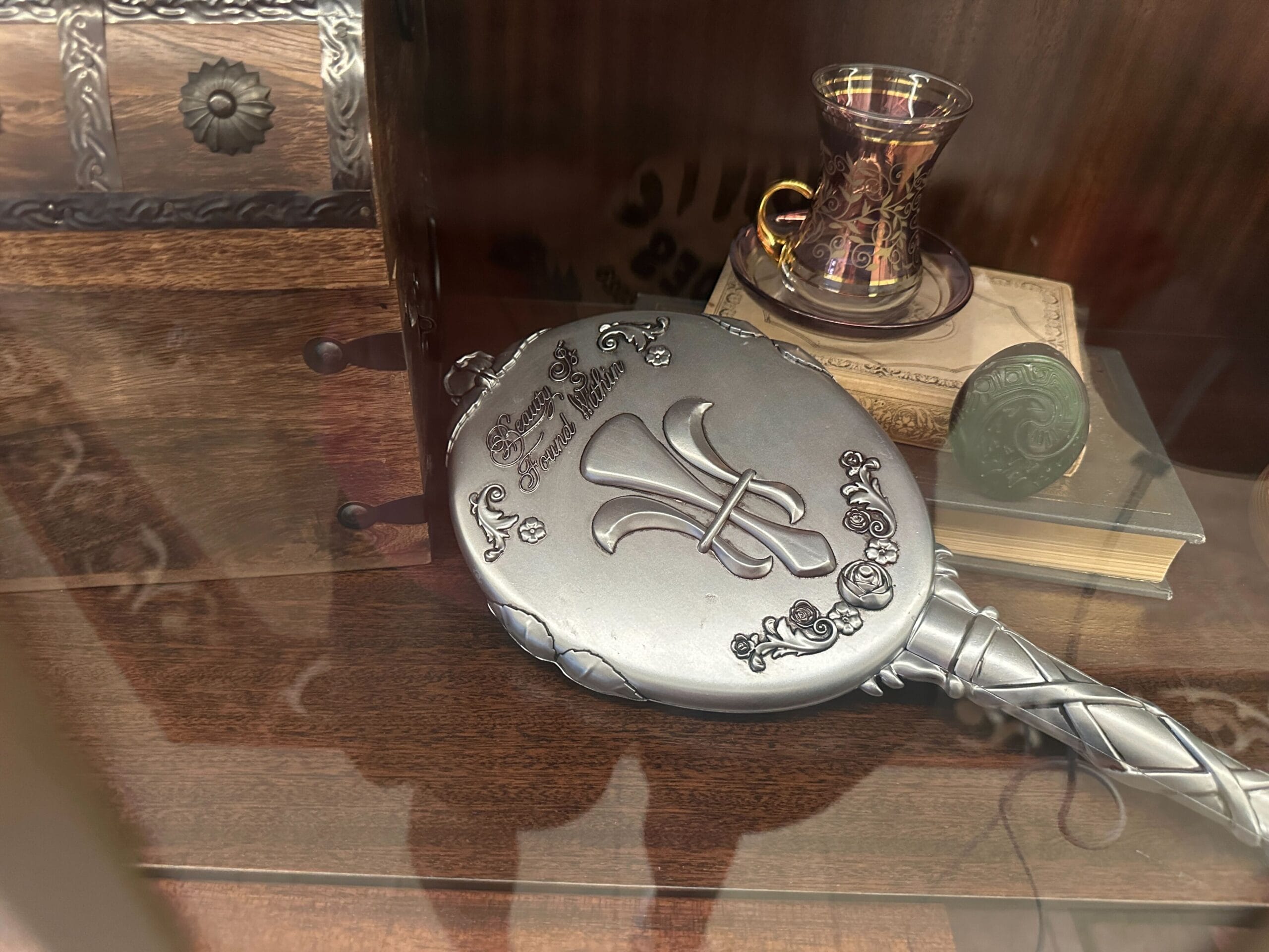An ornate silver hand mirror on a warm wood shelf in a glass-front display case in the refurbished Grand Floridian lobby bar. An ornate silver hand mirror on a warm wood shelf in a glass-front display case in the refurbished Grand Floridian lobby bar.