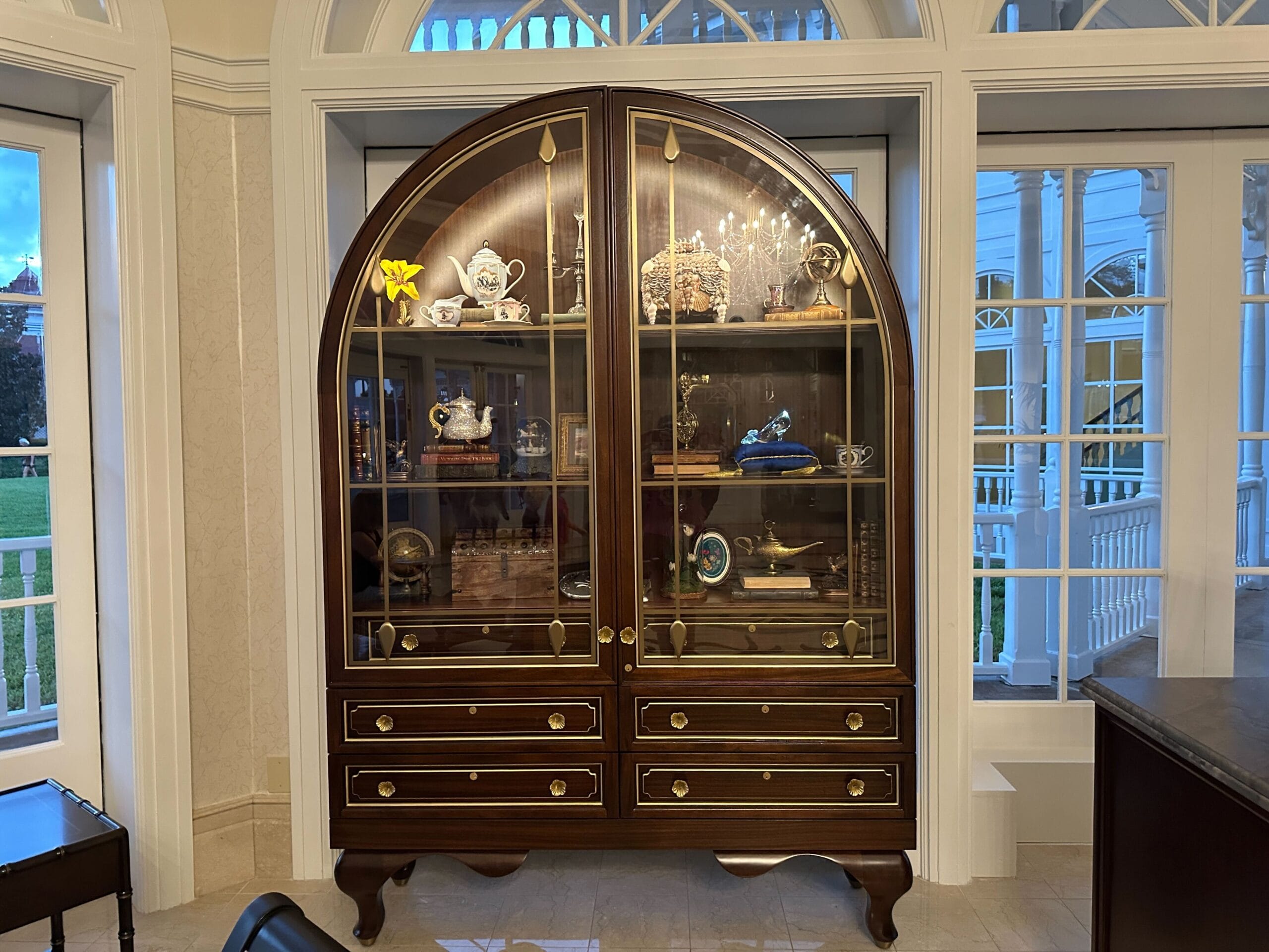 An arched dark wood cabinet with a glass front in the Grand Floridian lobby bar showcases homages to classic Disney films. An arched dark wood cabinet with a glass front in the Grand Floridian lobby bar showcases homages to classic Disney films.