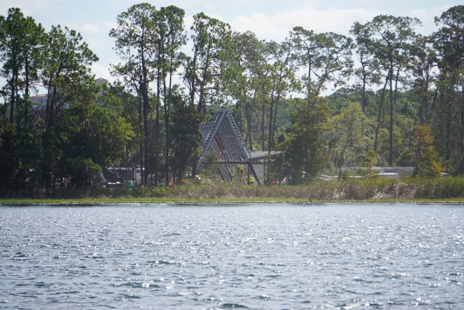 A triangular wooden structure stands among lakeside trees, reminiscent of Disney park architecture, across a shimmering lake. A triangular wooden structure stands among lakeside trees, reminiscent of Disney park architecture, across a shimmering lake.